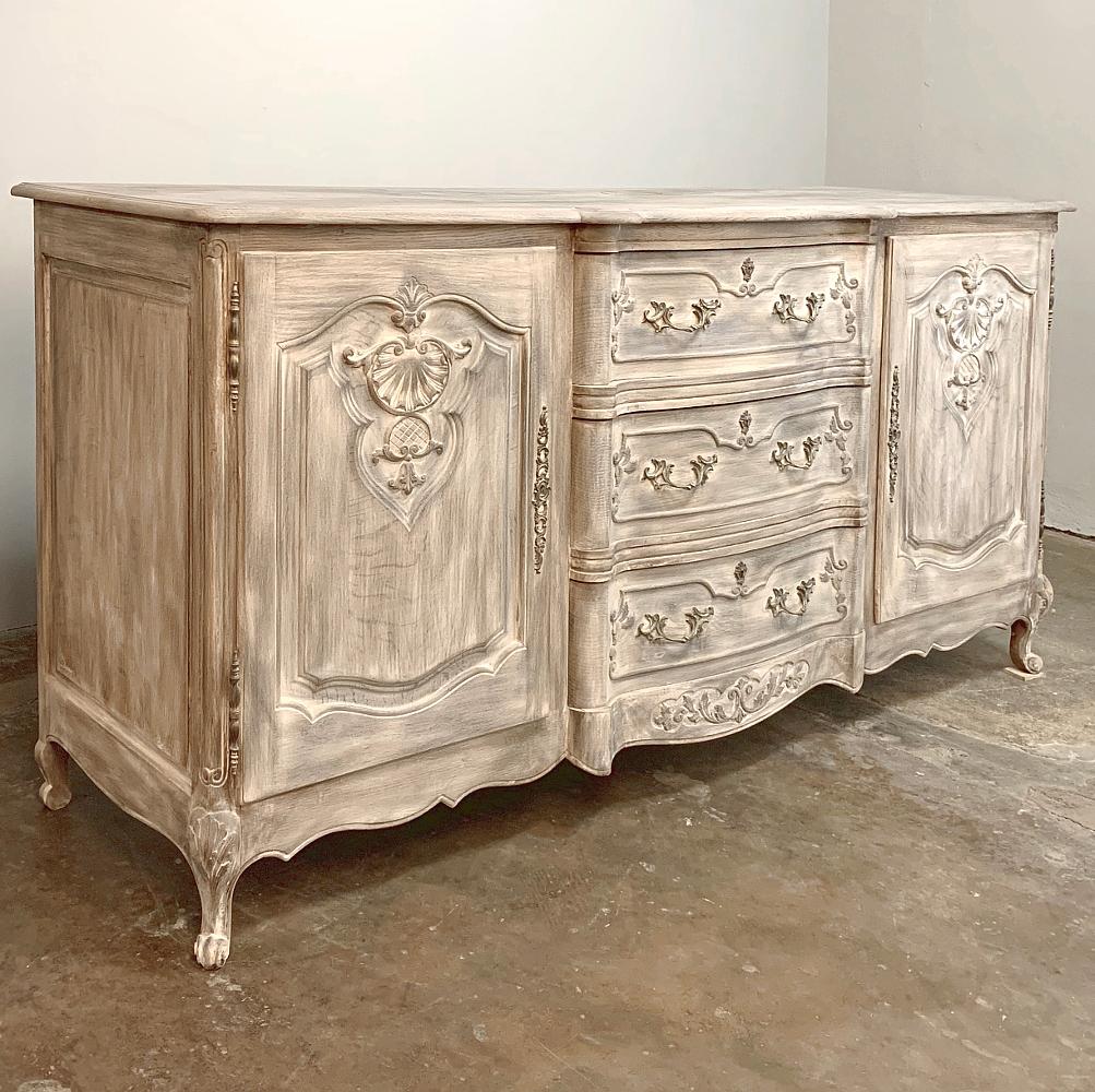 Antique French Louis XV whitewashed buffet is artistry in wood, with elegant molded detail providing a framework around the shell and stylized foliates on each door panel, and the Rococo cast brass drawer pulls at the center stepped-out section. The