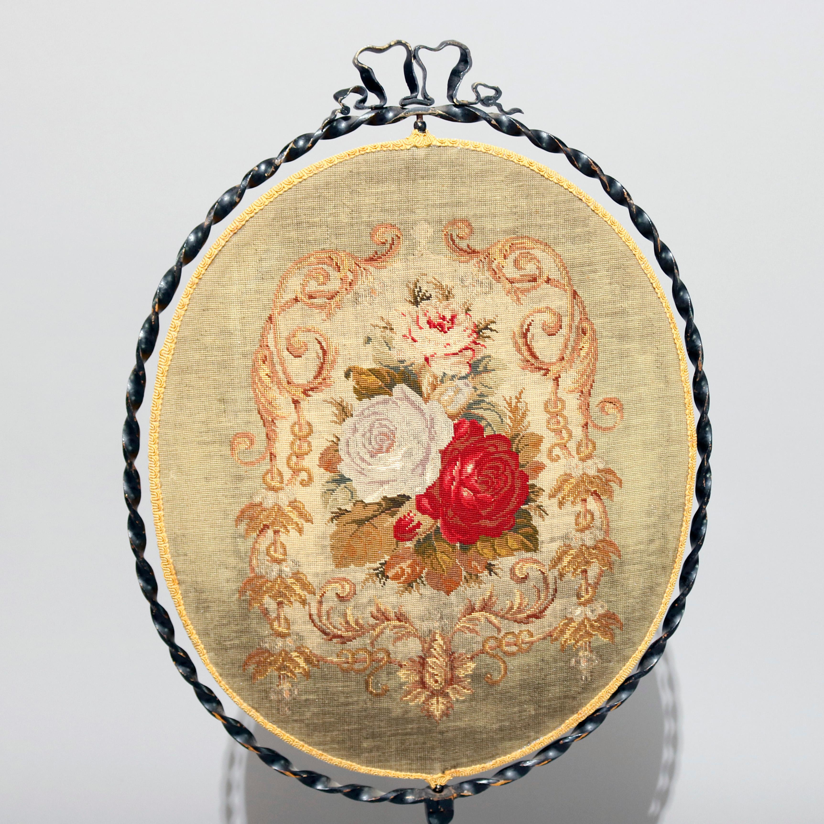 An antique French Louis XV fire screen features twisted wrought iron frame on tripod base with scroll form base, oval needlepoint in floral rose design swivels within frame, circa 1880

Measures - 42.5