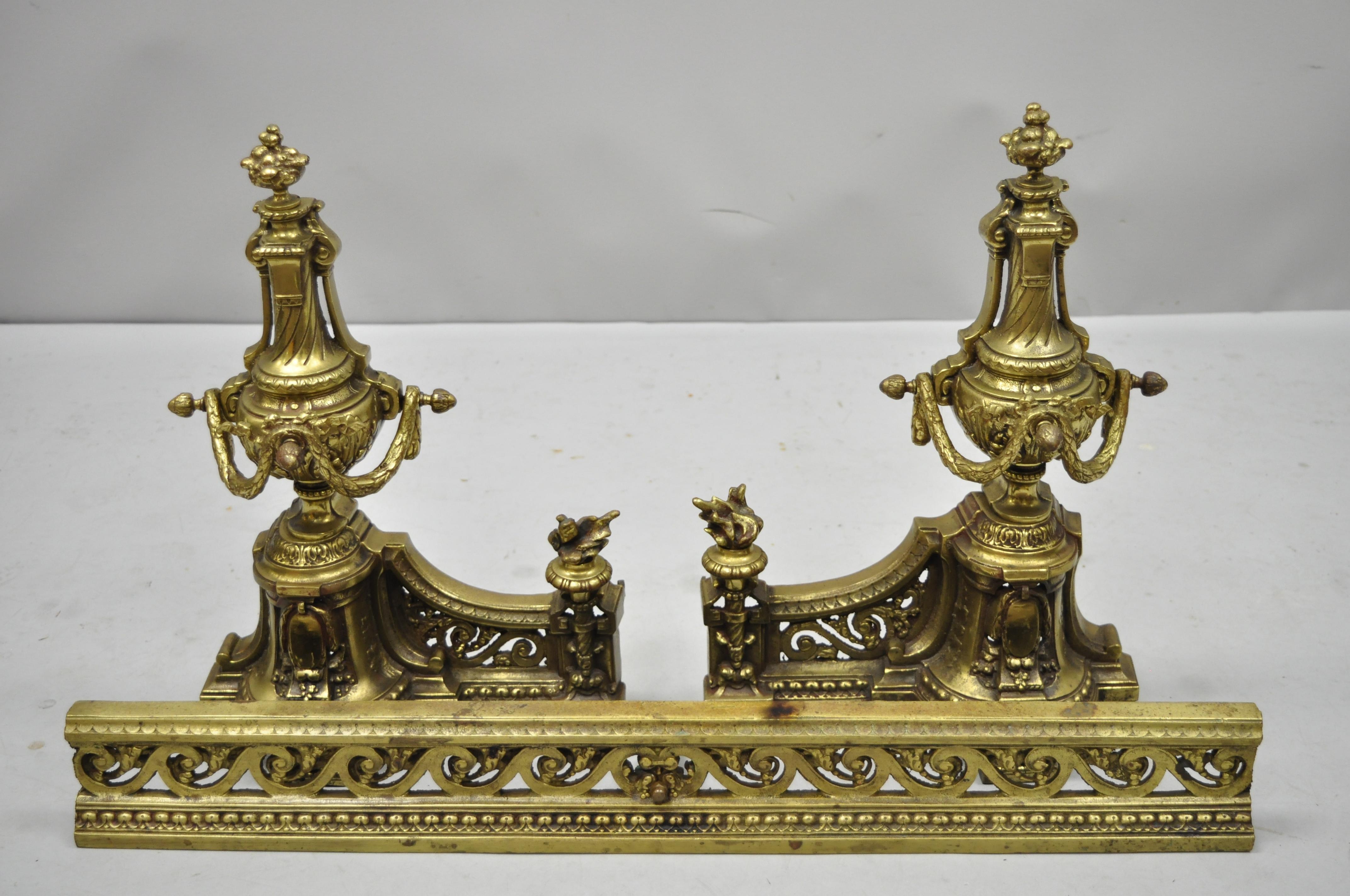 Antique French Louis XVI brass / bronze flame finial pair of andirons with adjustable fender. Item features pair of urn and flame finial andirons, pierced scrollwork fender, finely cast brass/bronze construction, great quality and form, circa early