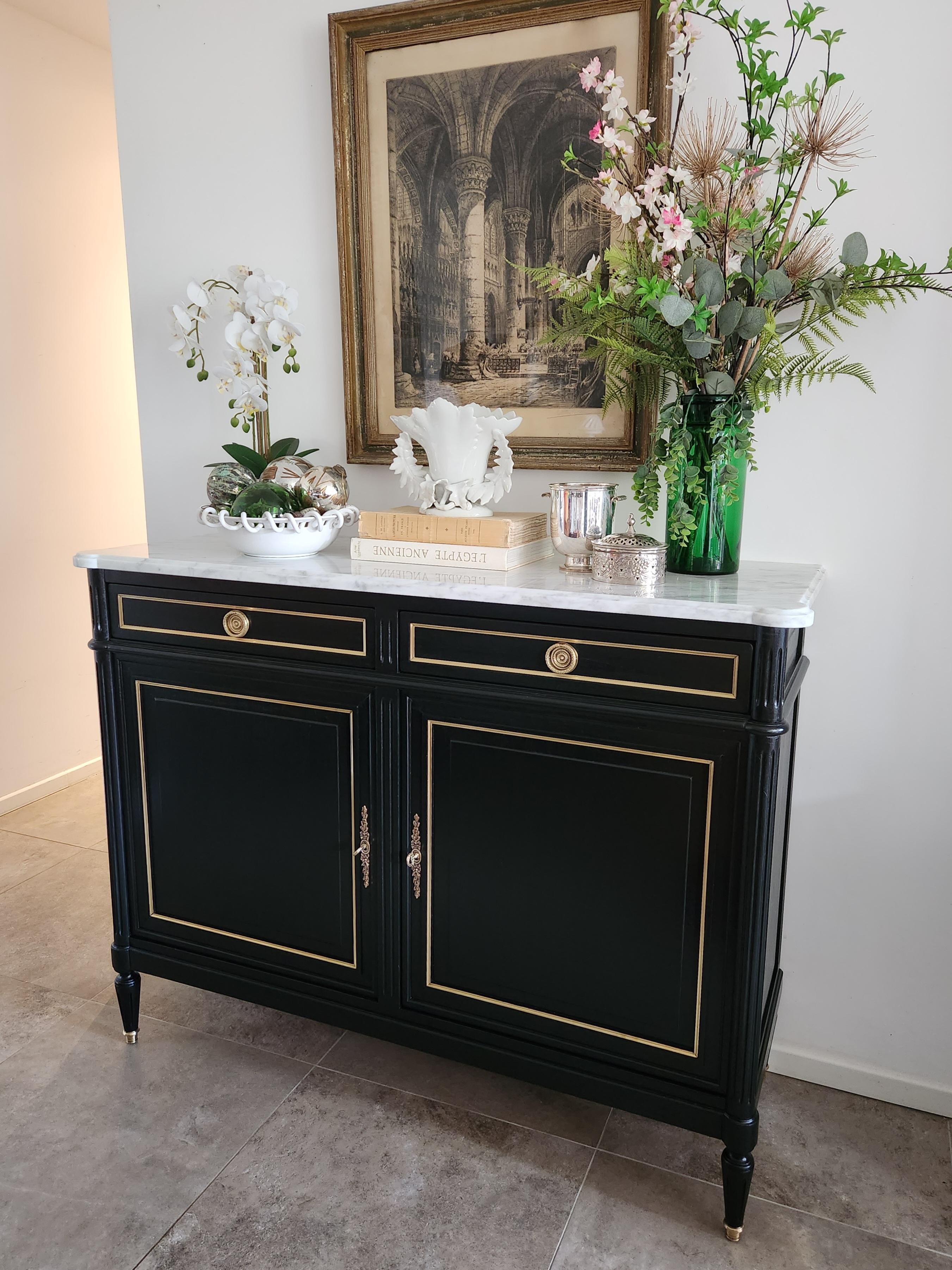 Antique French Louis XVI style sideboard topped with Carrara marble.
Comprising two doors with a height-adjustable shelf, two dovetailed drawers with gilt bronze handles, fluted legs, and gilt bronze sabots.

The cabinet is adorned with delicate