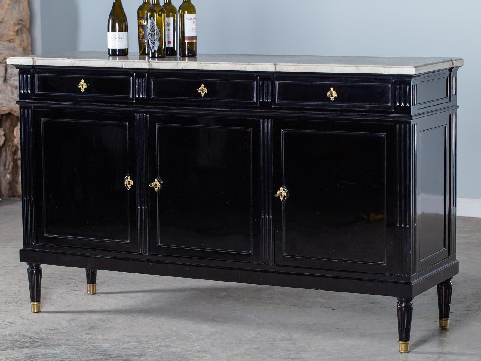 A stunning antique French Louis XVI style buffet credenza circa 1800 with its marble top and an ebonized black lacquer finish. The gilded handles and escutcheons gleam with a warm rich golden color and the brass caps on each foot have been polished