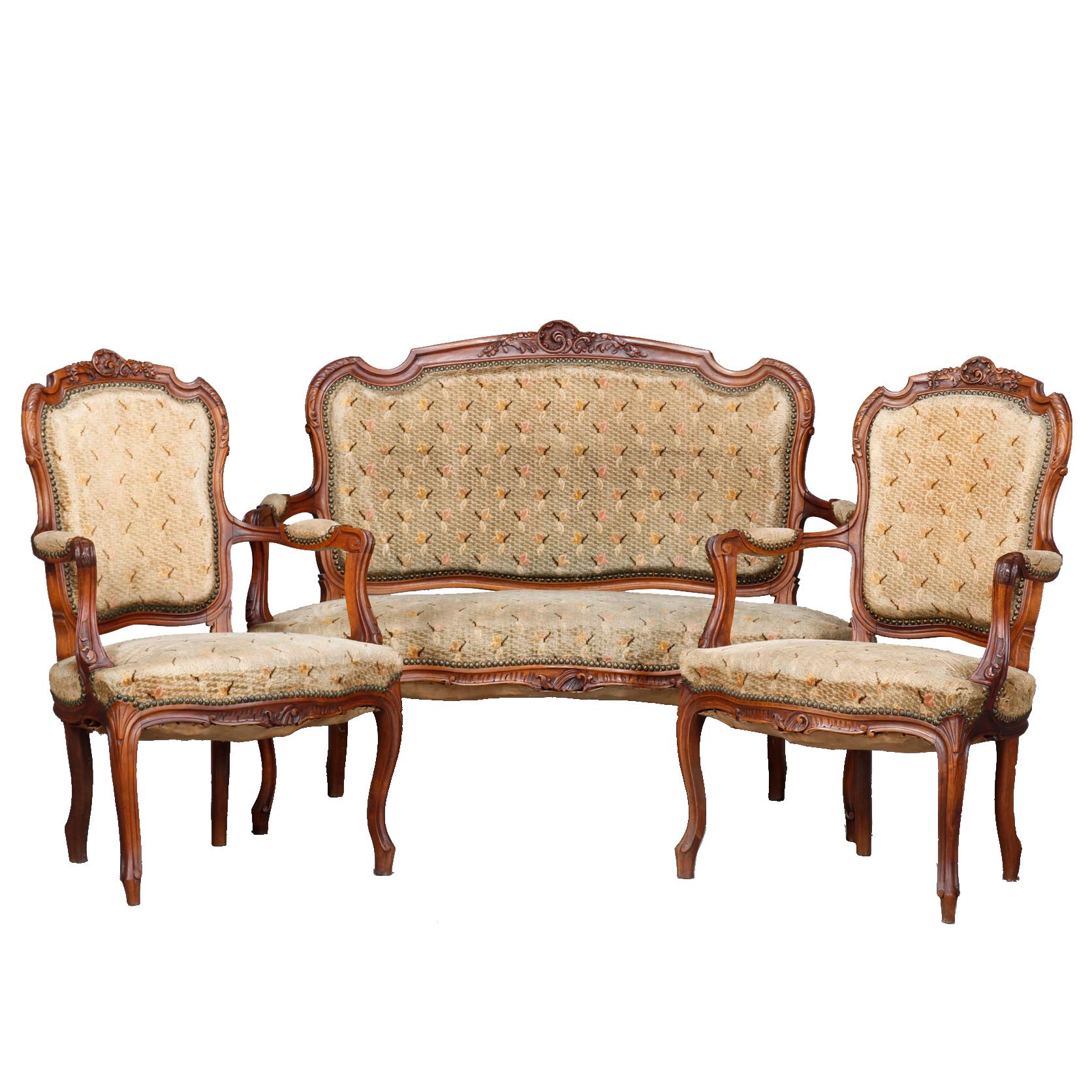 An antique French Louis XVI parlor set offers walnut construction with carved foliate crests, scroll arms and raised on cabriole les terminating in scroll feet; upholstered backs, seats and arms; set includes settee with two arm chairs, circa