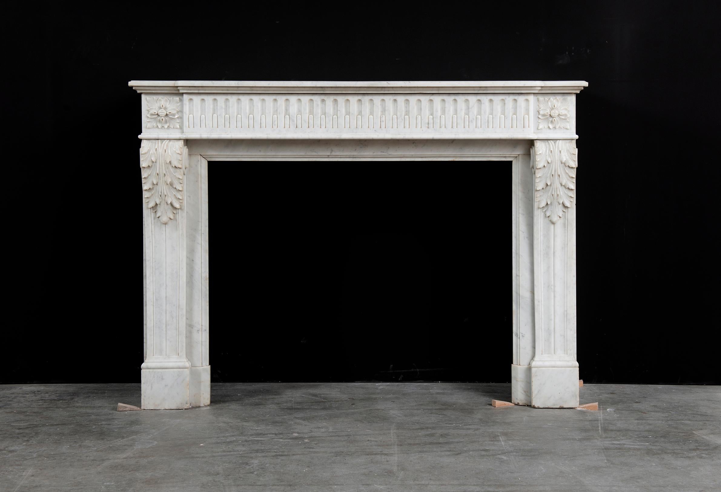 Happy to offer this very pleasing Louis XVI fireplace mantel in Carrara white marble. 

The moulded breakfront shelf sits above a stop fluted frieze that end in acanthus paterae endblocks on both sides. These enblocks rest on beautifully carved