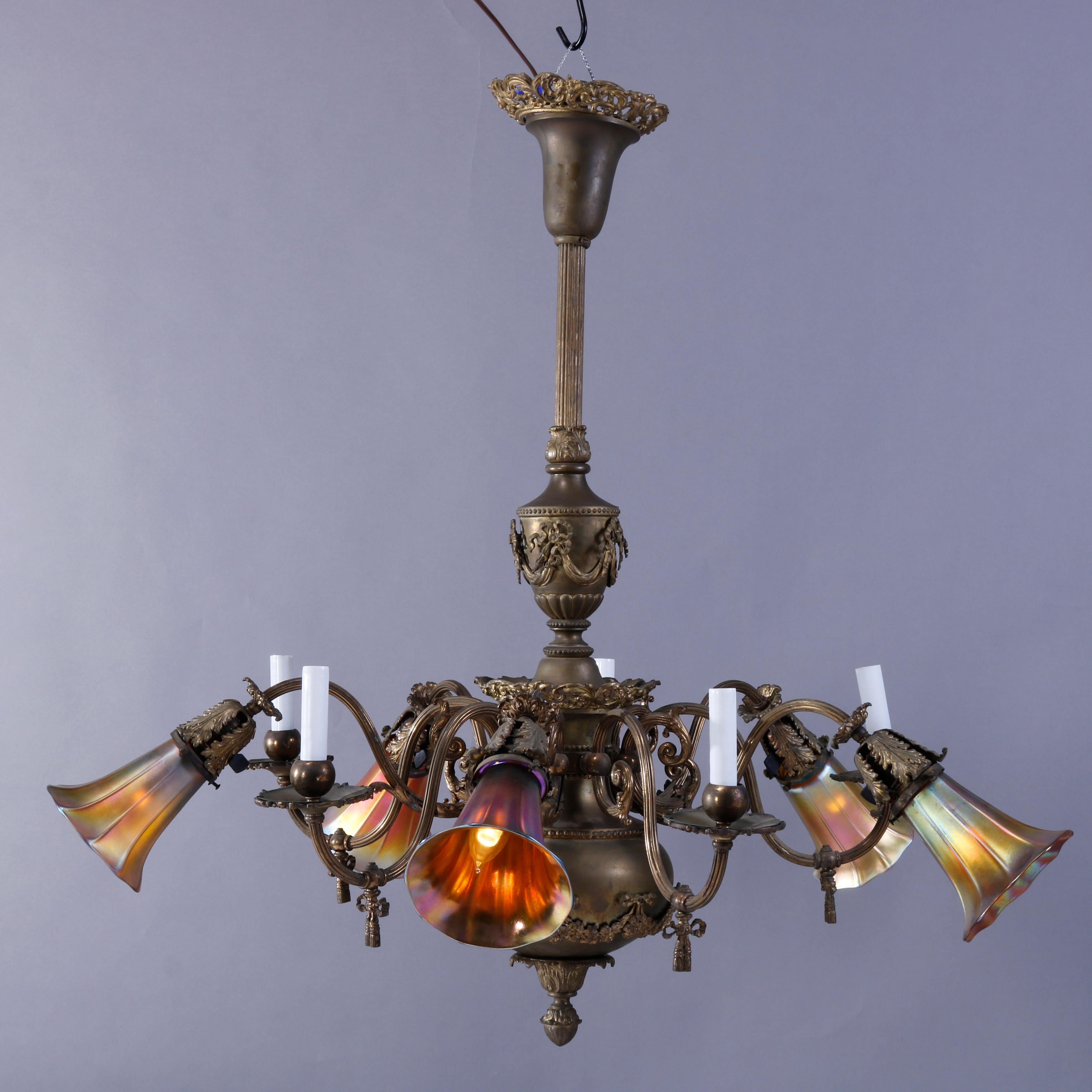 An antique French Louis XVI gas and electric chandelier offers brass and bronze construction with reeded shaft over chandelier with swag and foliate elements, having five scroll form arms terminating in drop lights having art glass aurene shades,
