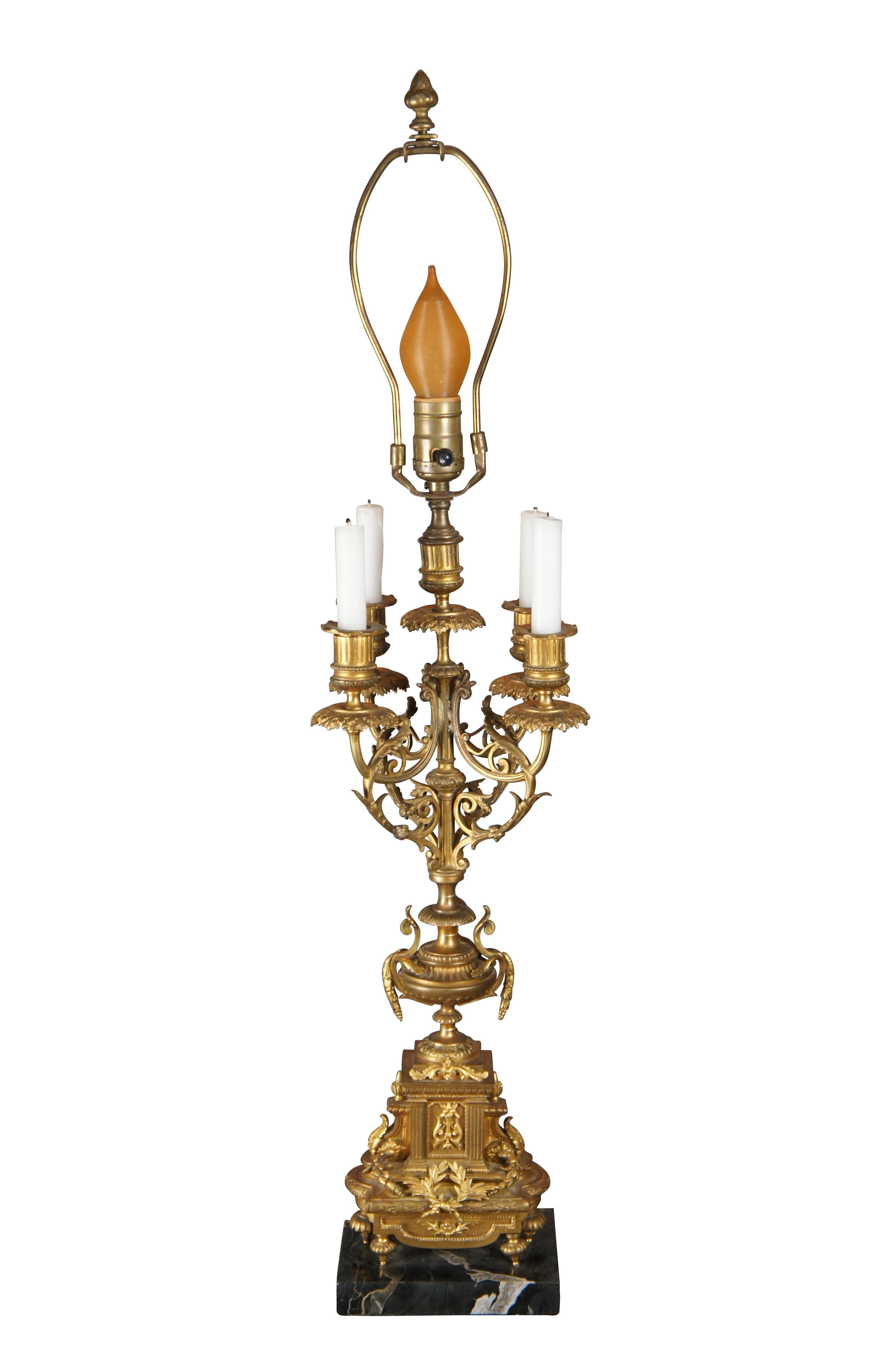 An elegant French Louis XVI Converted Candelabra Lamp. Features a gilt brass finish with classical motifs over a footed base on a black marble plinth. Arms are scrolled with acanthus accents and ornate drip pans. Lamp was added at the center where