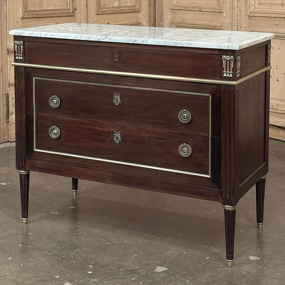 Antique French Louis XVI Mahogany Commode with Carrara Marble è un esempio insolitamente elegante del genere!  Il marmo di Carrara, con le sue lussuose venature, è una superficie espositiva perfetta.  Direttamente sotto, il piano superiore è