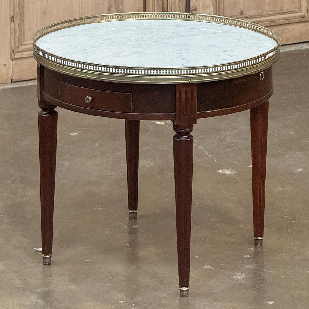 Antique French Louis XVI Mahogany Marble Top Bouillotte Table represents an understated elegance that is perfect for the tailored yet refined decor. Hand-crafted from exotic imported mahogany, it features a round apron interrupted by fluted plinth