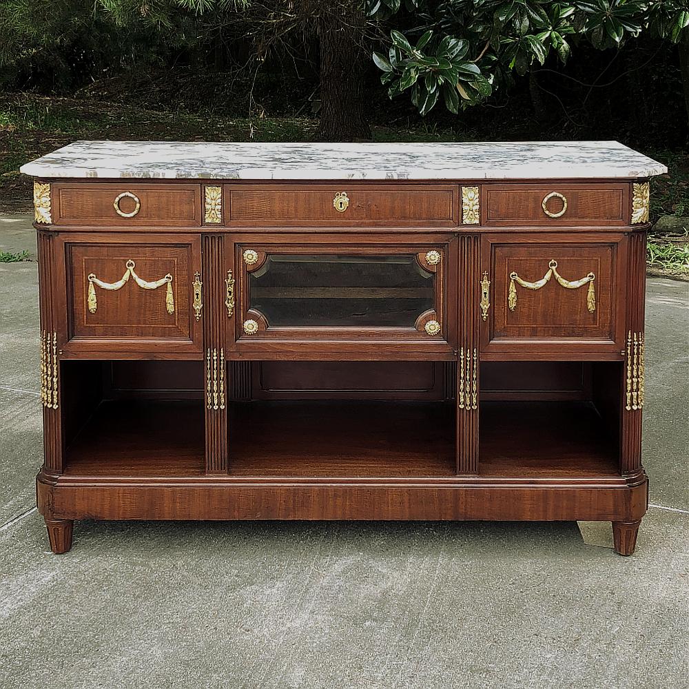 L'Antique French Louis XVI Mahogany Top Buffet with Gilt Bronze Mounts rappresenta l'essenza dello stile classico celebrato soprattutto negli ultimi anni del XIX secolo fino ai giorni nostri. Questo esemplare, realizzato in mogano esotico importato,