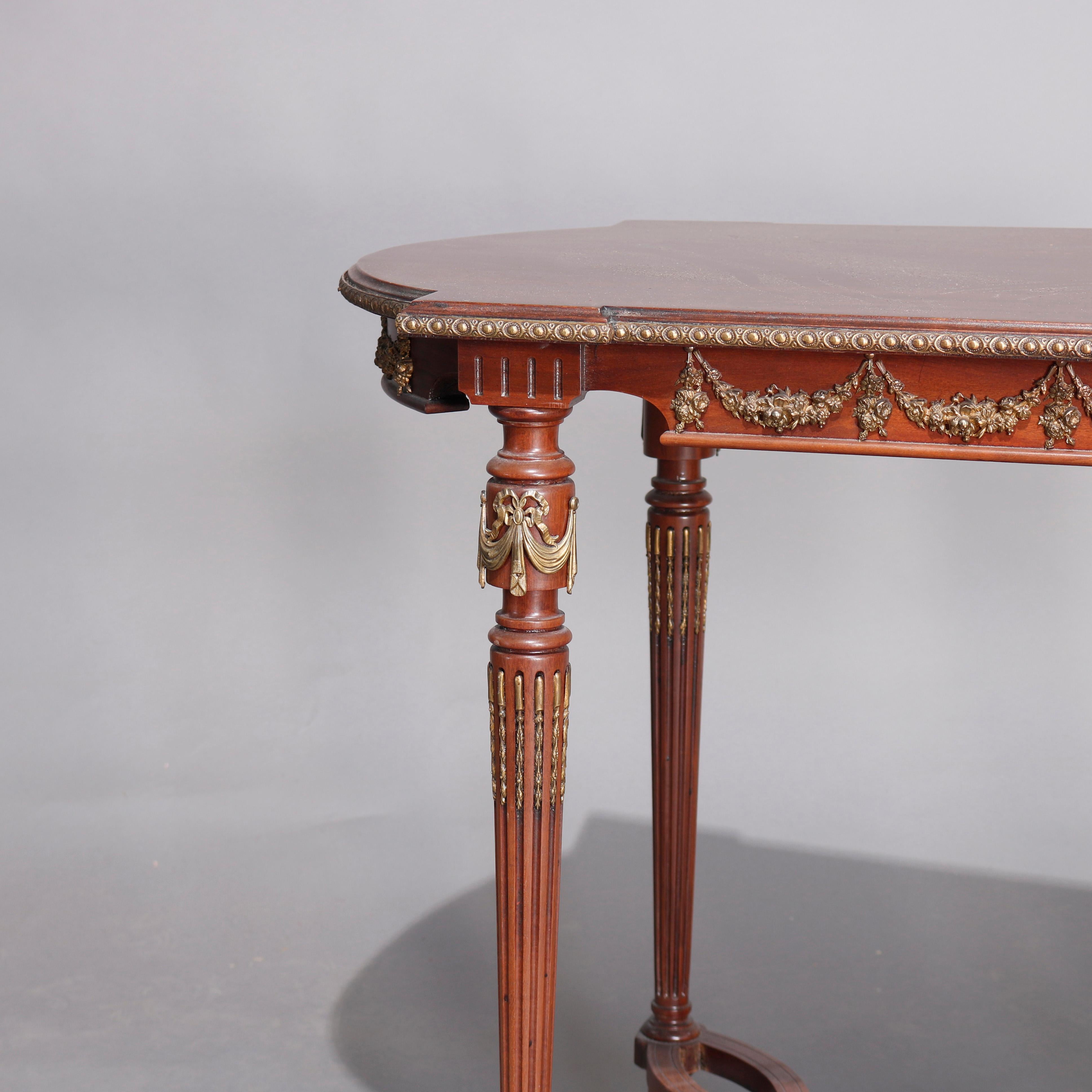 An antique French Louis XVI side table offers mahogany construction with shaped top surmounting apron having foliate garland banding and mounts, raised on reeded and tapered legs with scroll form lower shelf, ormolu mounts and insets throughout,