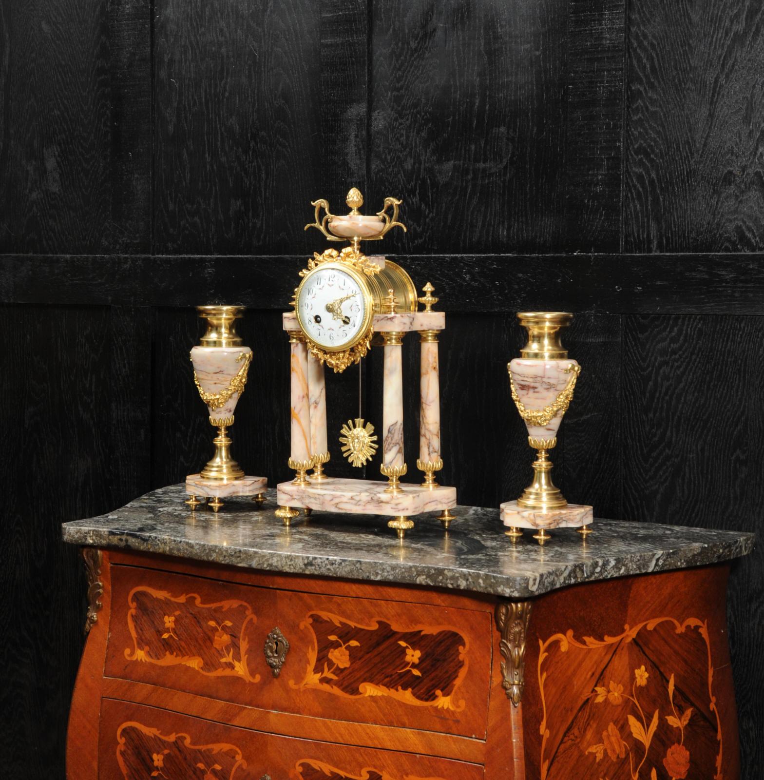 A beautiful antique French portico clock set, circa 1900. It is of Louis XVI style and made of a stunning variegated specimen marble, mounted with ormolu (finely gilded bronze). The marble is veined with oranges, pinks, violets and blues. The