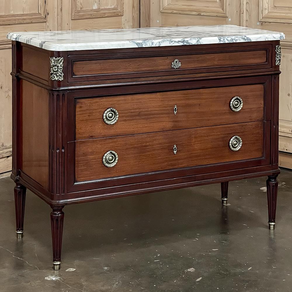 Antique French Louis XVI Neoclassical Marble Top Mahogany Commode is a timeless expression of the architecture and style that dates back to the ancient Greek and Roman civilizations. Using two tones of exotic imported mahogany, a darker oxblood red