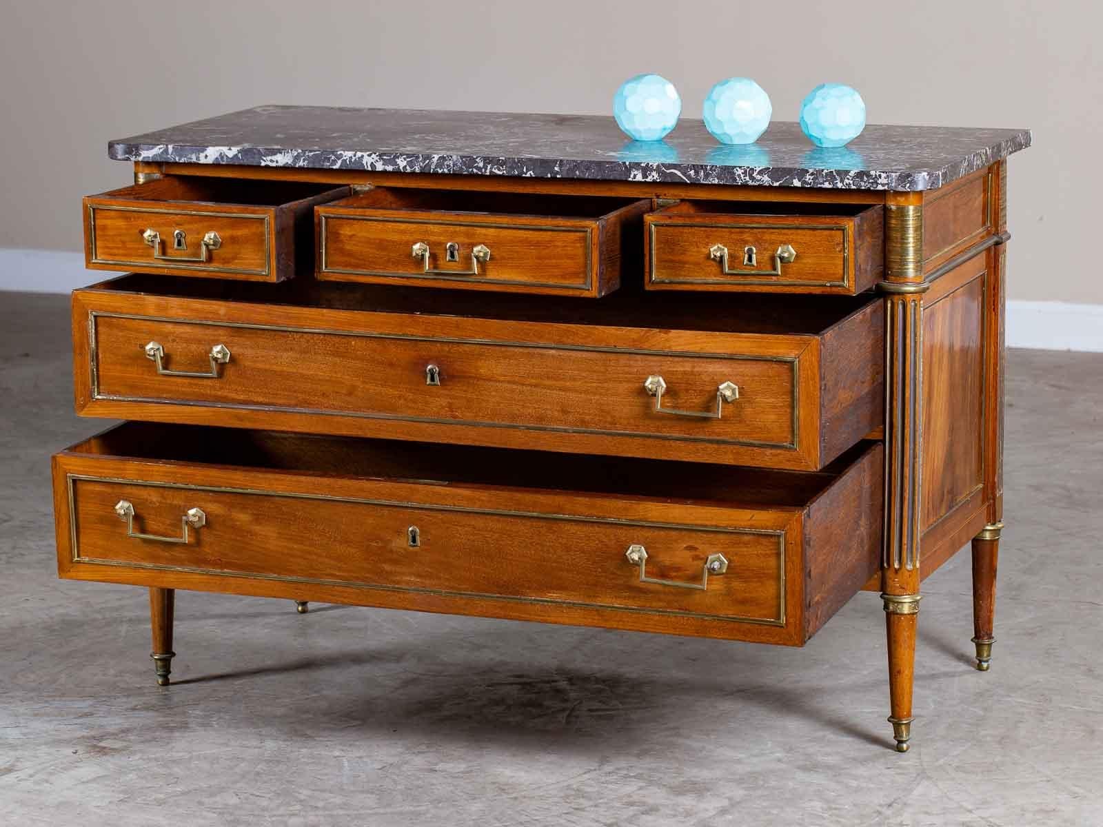 This Neoclassical Louis XVI period antique French walnut commode chest, circa 1790 has a marble top along with five drawers all embellished with brass detailing. The elegant simplicity of this late 18th century French chest of drawers results from