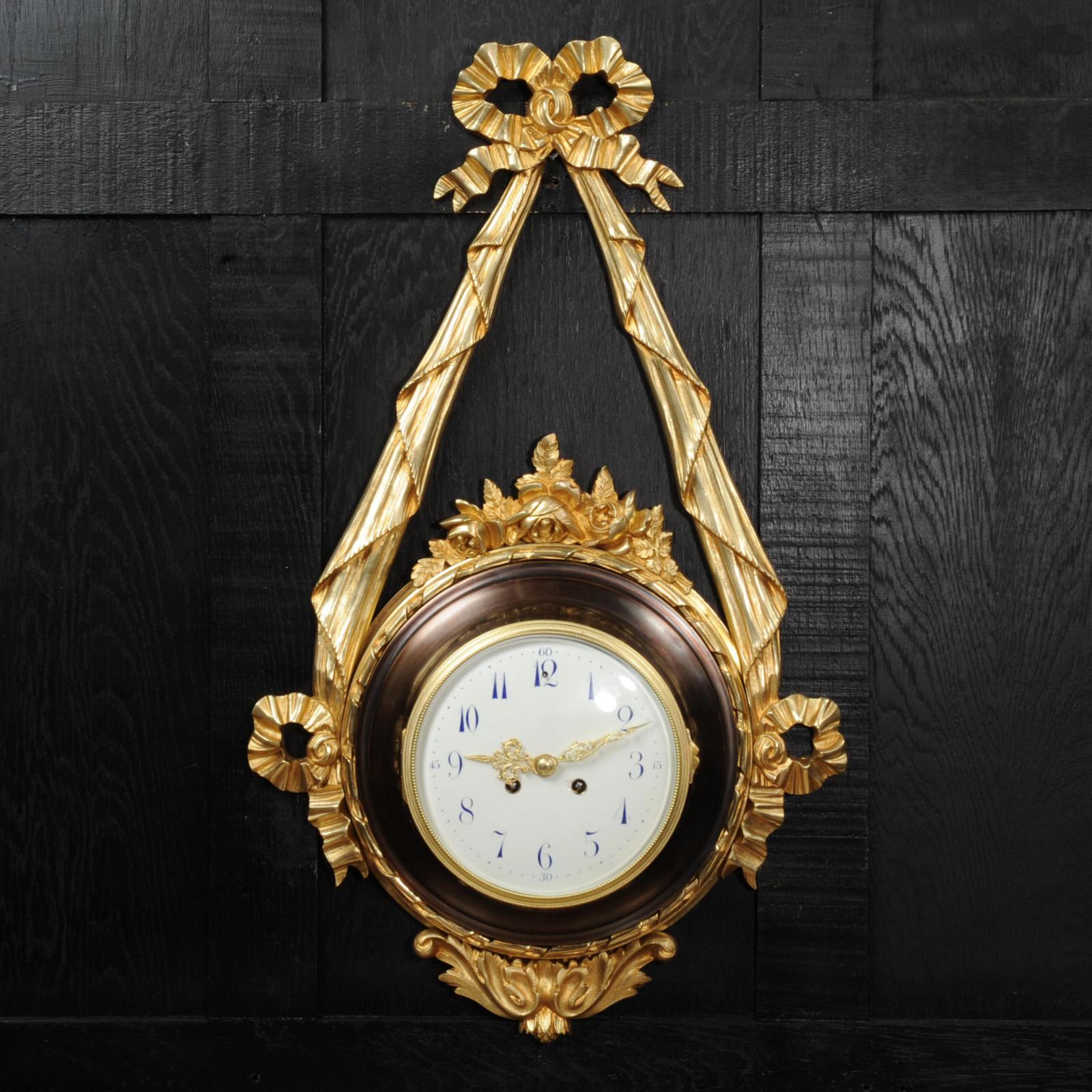 A superb and very large cartel wall clock in the style of Louis XVI, circa 1880. It is formed as a round bronze body housing the movement suspended from an ormolu ribbon swag with a bow crest. The bronze body has decorations of roses to the top and