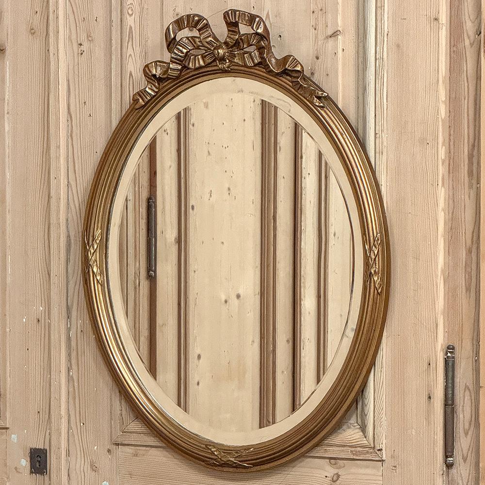 Ce miroir mural ovale en bois doré de style Louis XVI fera un bel effet dans n'importe quelle pièce, en particulier dans la salle d'eau !  Fabriqué avec un magnifique cadre de blé bandé sur tout le pourtour, surmonté d'un ruban fluide noué en un
