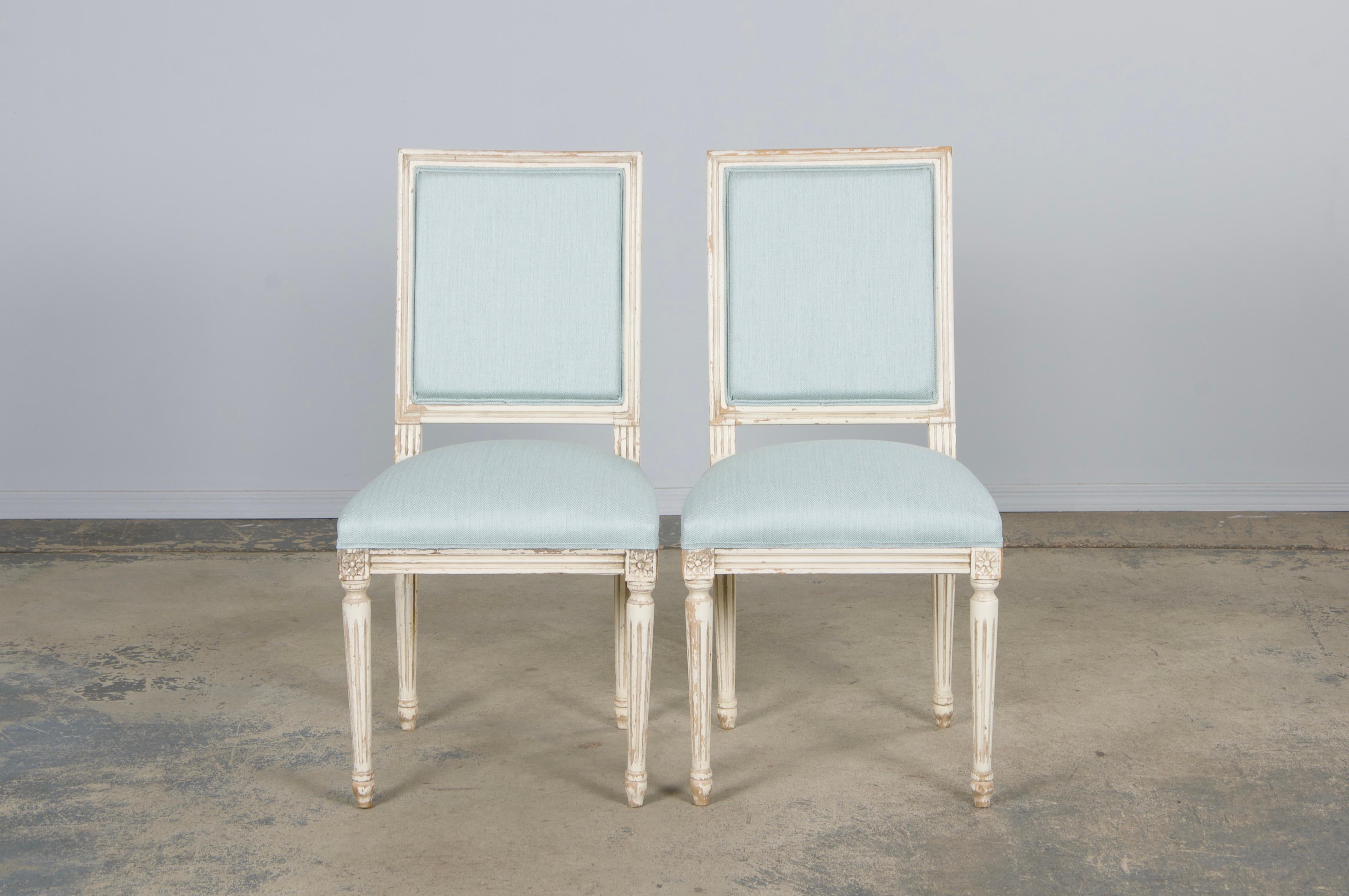 A charming pair of late-19th-century Louis XVI-style accent chairs, sourced from Provence, France. Each features a hand-crafted maple frame with a square back, hand-painted in creamy antique white with a naturally distressed patina revealing hints