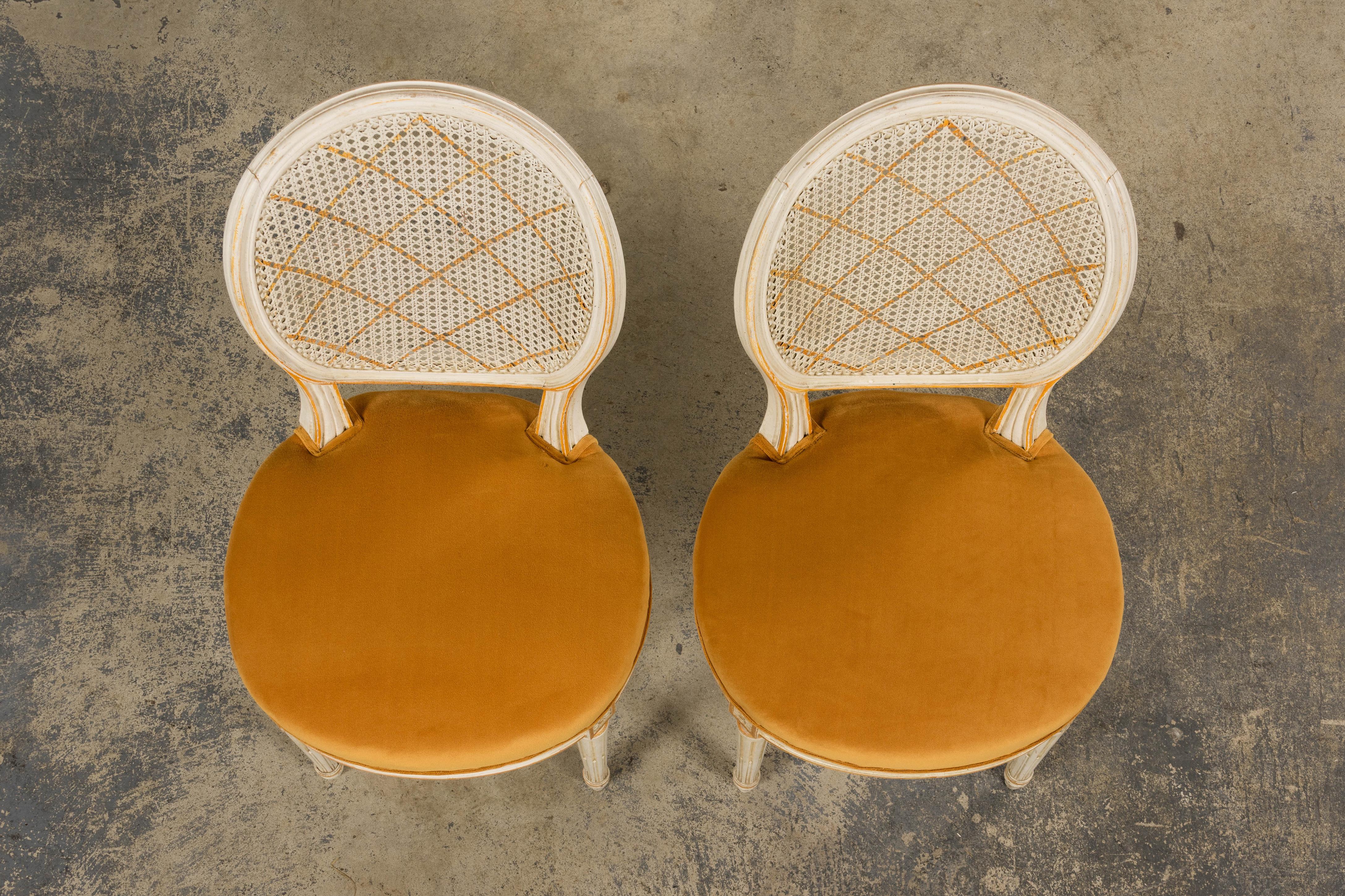 A refined pair of late 19th-century Louis XVI-style accent chairs, sourced in Provence and newly upholstered in sumptuous marigold velvet by Scalamandré. Each features an intricately hand-carved frame with oval cane backs, fluted legs, and rosette