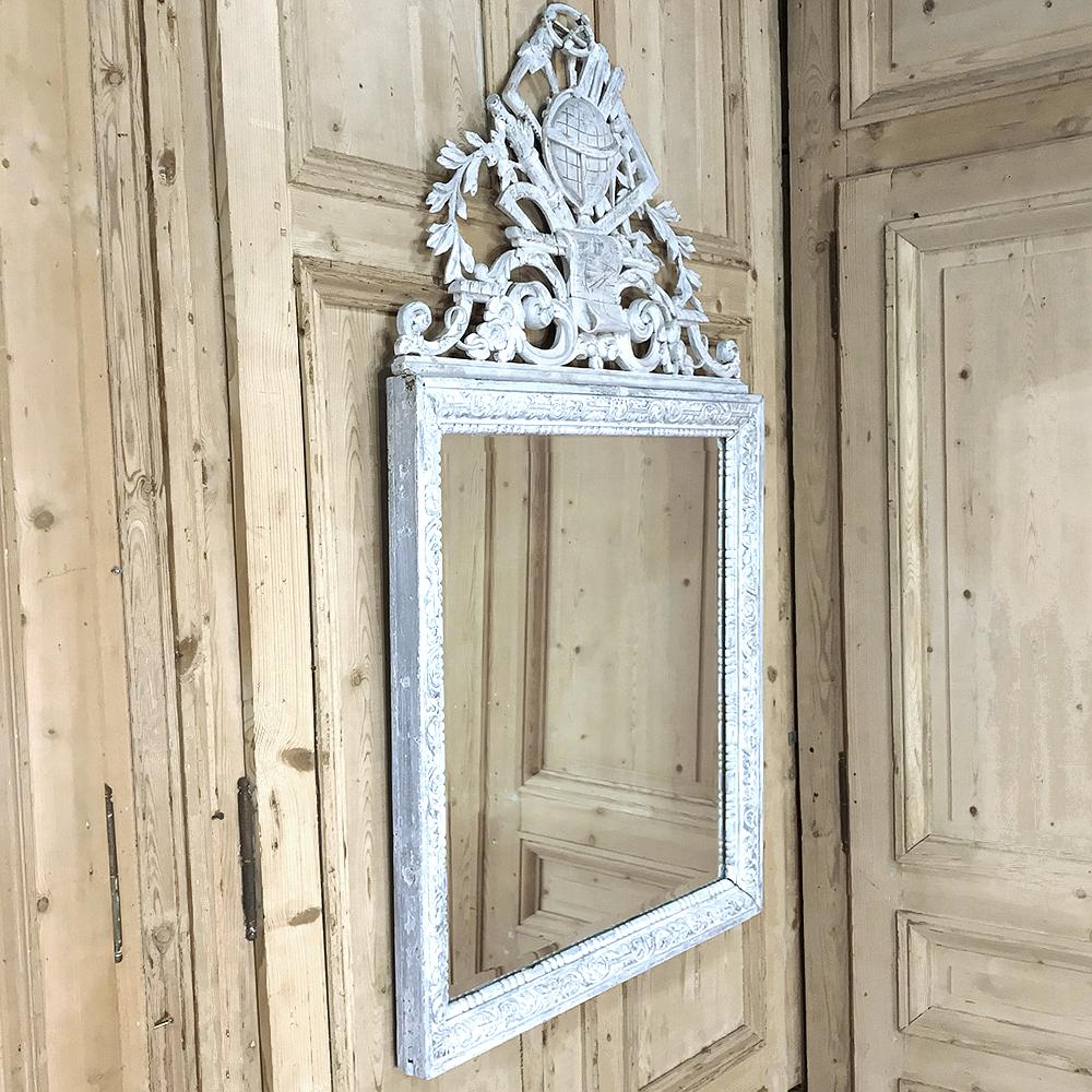 Antique French Louis XVI painted mirror features a glorious display of sculpture on top with a lovely patinaed painted finish that creates a timeless look. Intriguing motifs have been pierce-carved across the crown, representing cartography, world