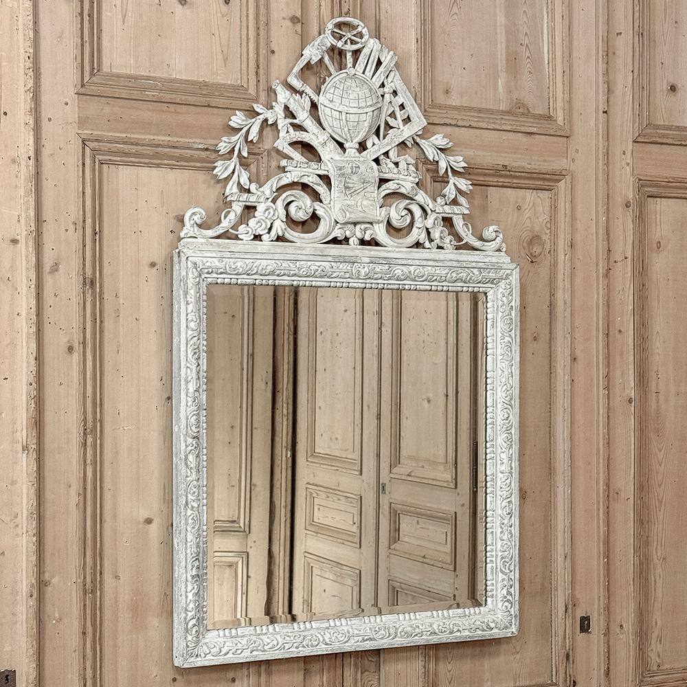 19th Century French Louis XIV Painted Mirror features a glorious display of sculpture on top with a lovely patinaed painted finish that creates a timeless look.  Intriguing motifs have been pierce-carved across the crown, representing cartography,