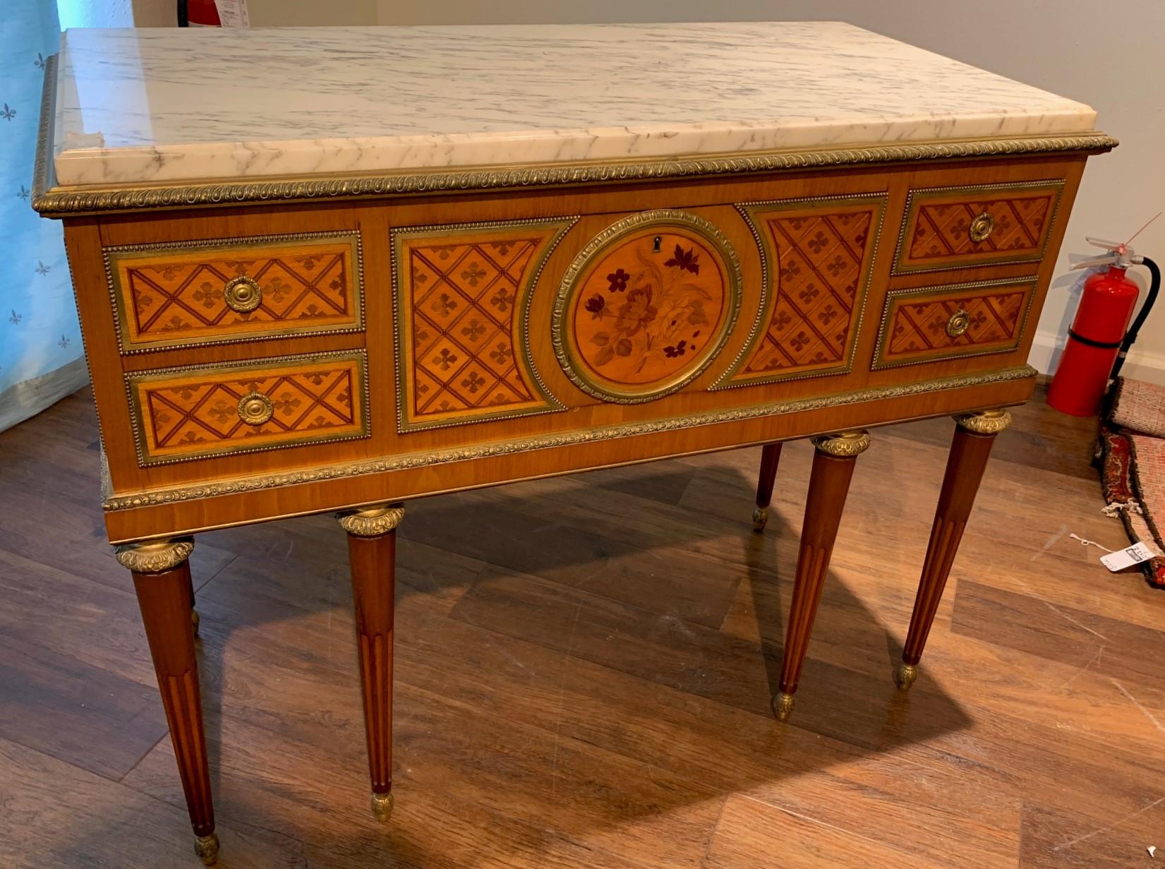 Outstanding antique French parquetry inlaid commode with a very thick and fine quality marble top. Exhibiting superb gilt bronze trim and a central panel inlaid with a floral bouquet utilizing a variety of woods. The entire on Classic Louis XVI