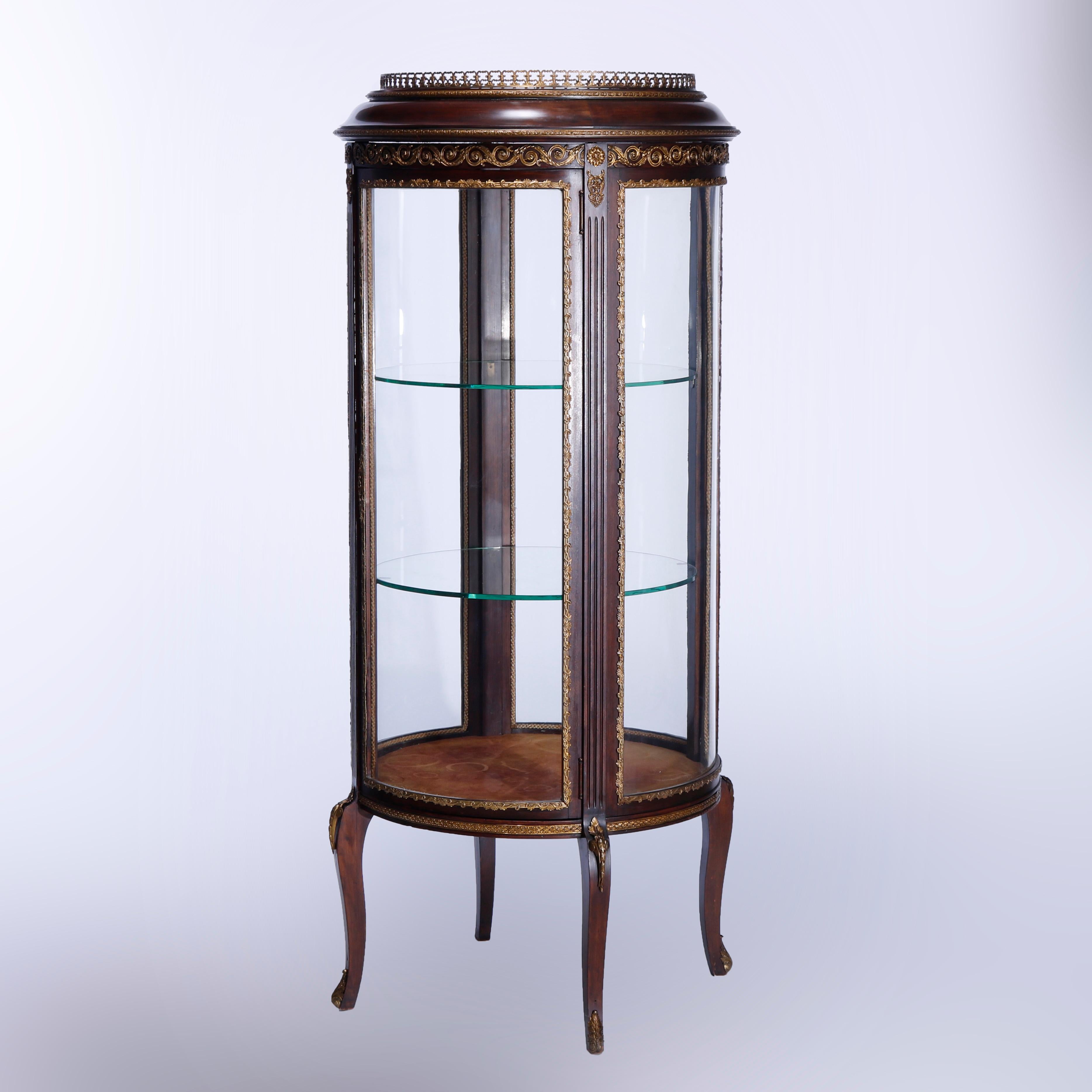 An antique French Louis XVI vitrine offers cast pierced gallery surmounting flame mahogany case in cylindrical form having curved glass, single door opening to shelved interior, cast foliate ormolu throughout, reeded columns, and raised on cabriole