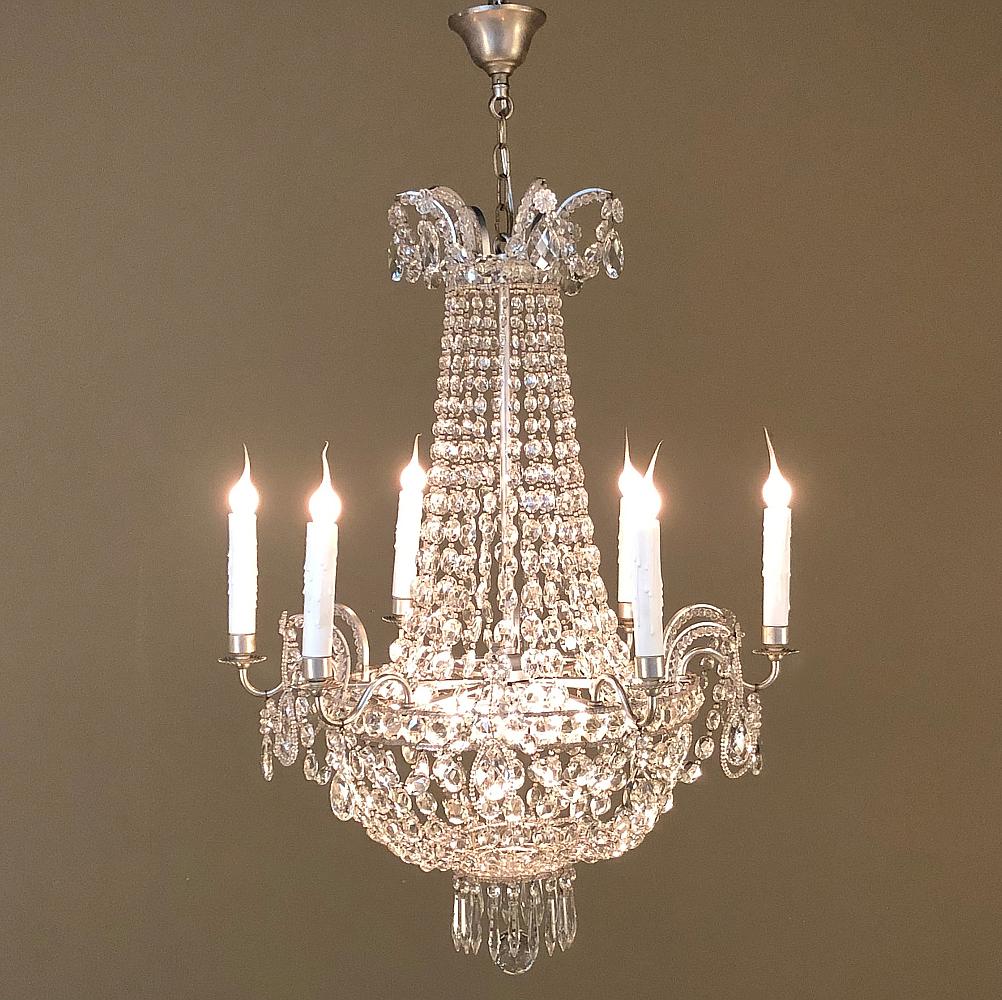 Der antike französische Louis XVI-Kronleuchter mit Perlenkette ist ein Wunderwerk der Kristallkunst! Die Architektur besteht aus gebürstetem Stahl und umfasst das passende Original-Vordach. Direkt unter dem Baldachin erscheint die Krone mit
