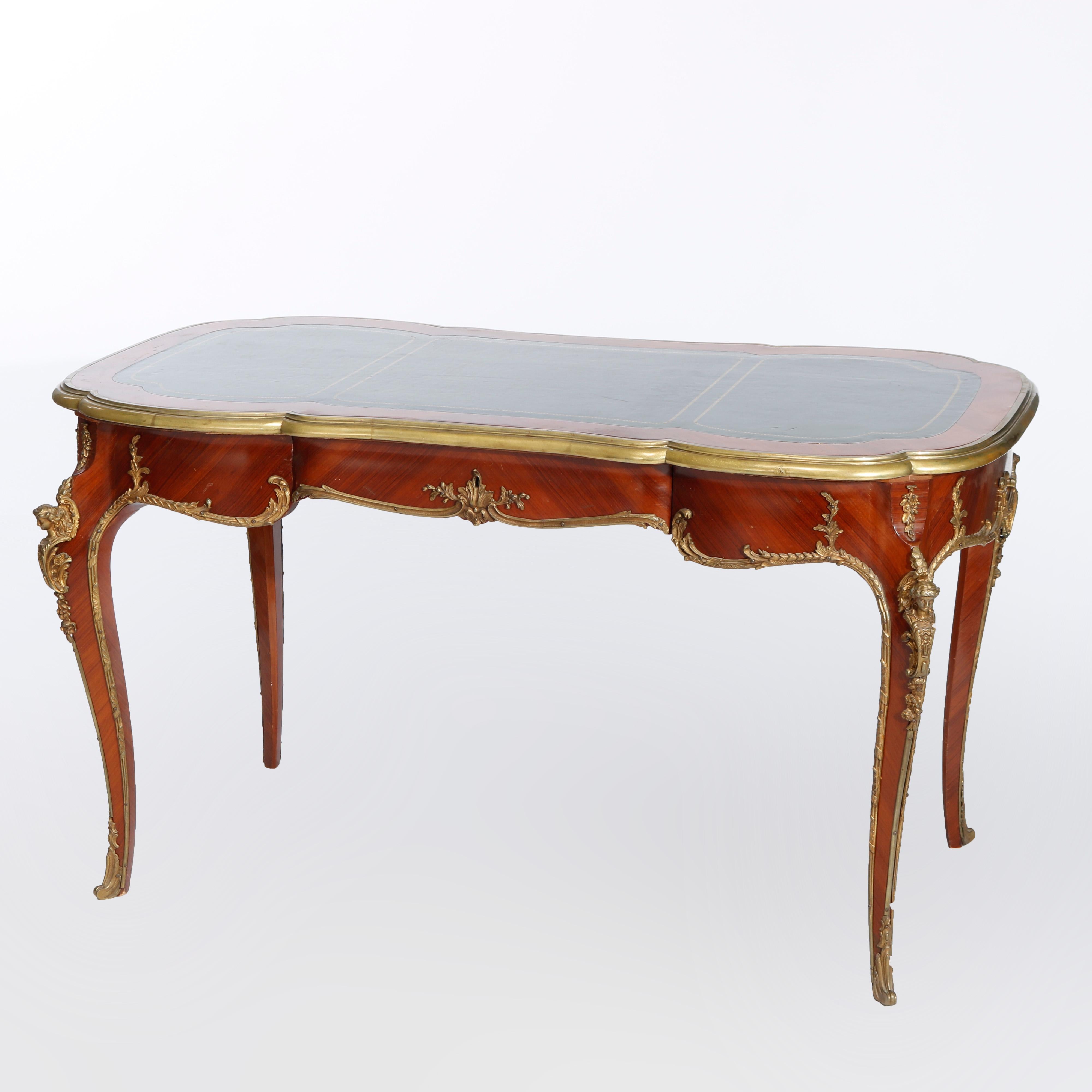 An antique French Louis XVI style bureau plat writing desk offers satinwood construction with shaped top having gilt-decorated leather writing surface on case with bookmatched facing, single central drawer, raised on cabriole legs with figural