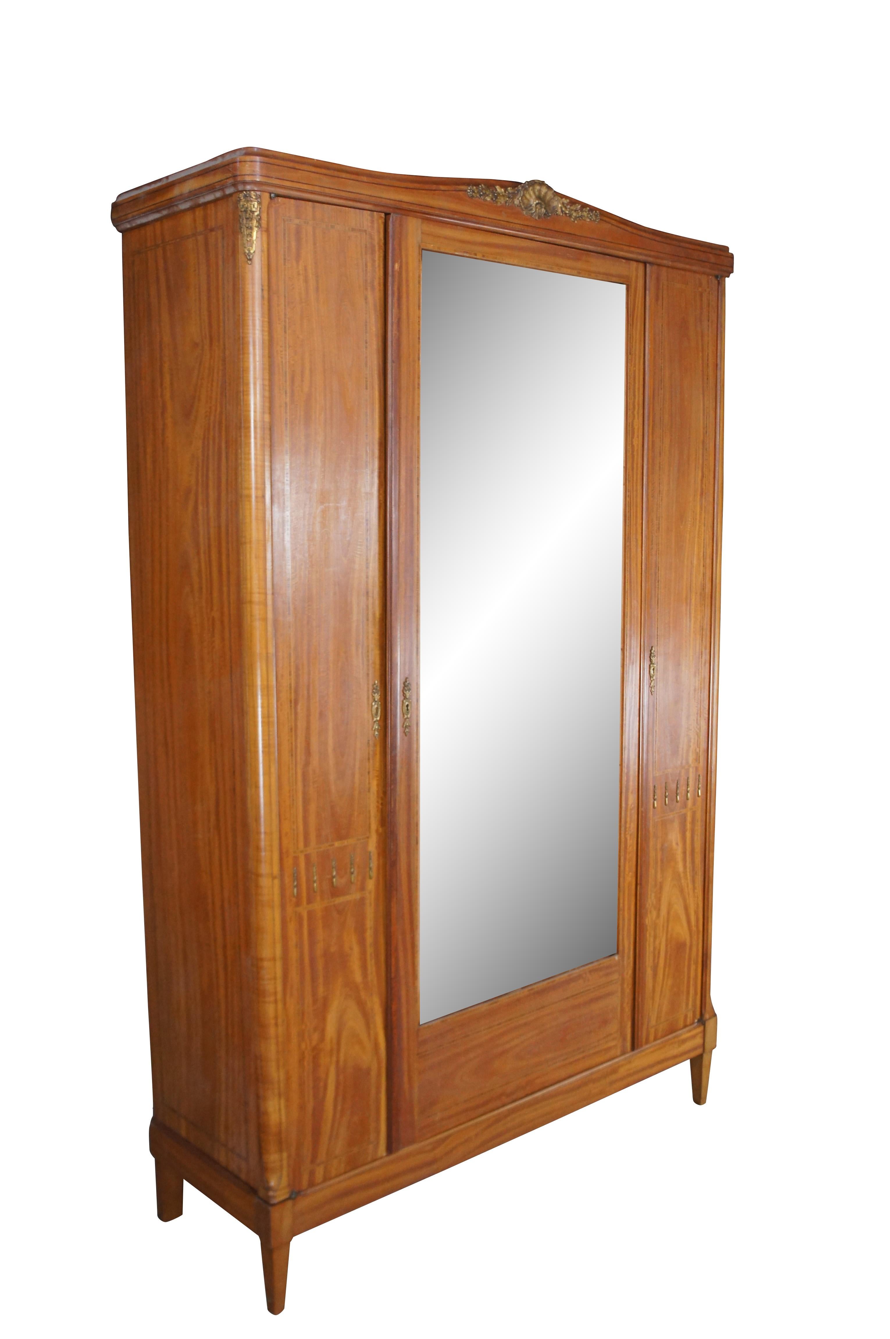 Antique French Louis XVI Style Armoire, circa last quarter 19th century.  Made from satinwood with crossbanding, a large central mirror flanked by columns, a scalloped crown and ormolu accents. The wardrobe opens to three adjustable shelves and two