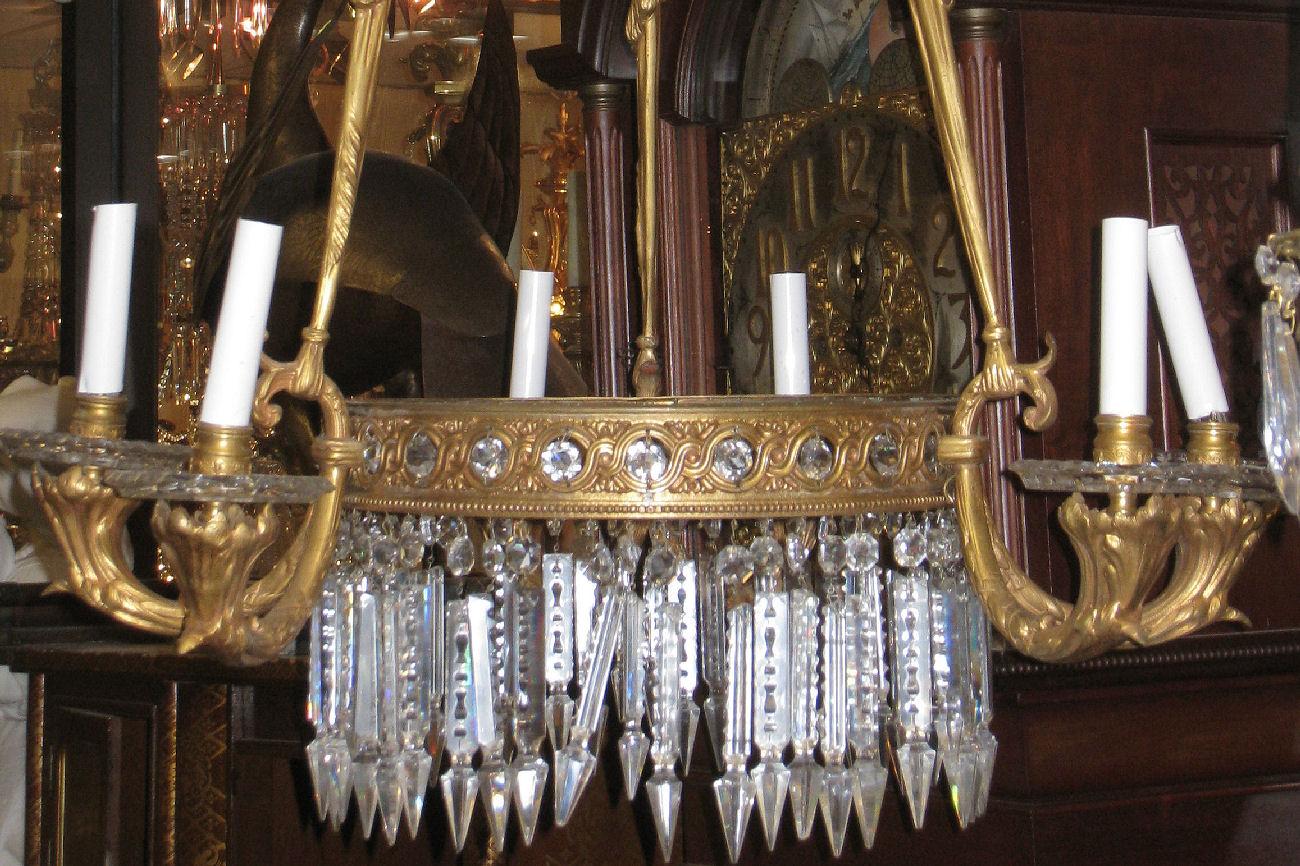 Lustre ancien (19e siècle) en bronze de style néoclassique français Louis XVI avec anneau central réticulé à motif guilloché et pendentifs en cristal, six bras de bougie émanant de bras à volutes soutenus par trois supports de style drapé, suspendus