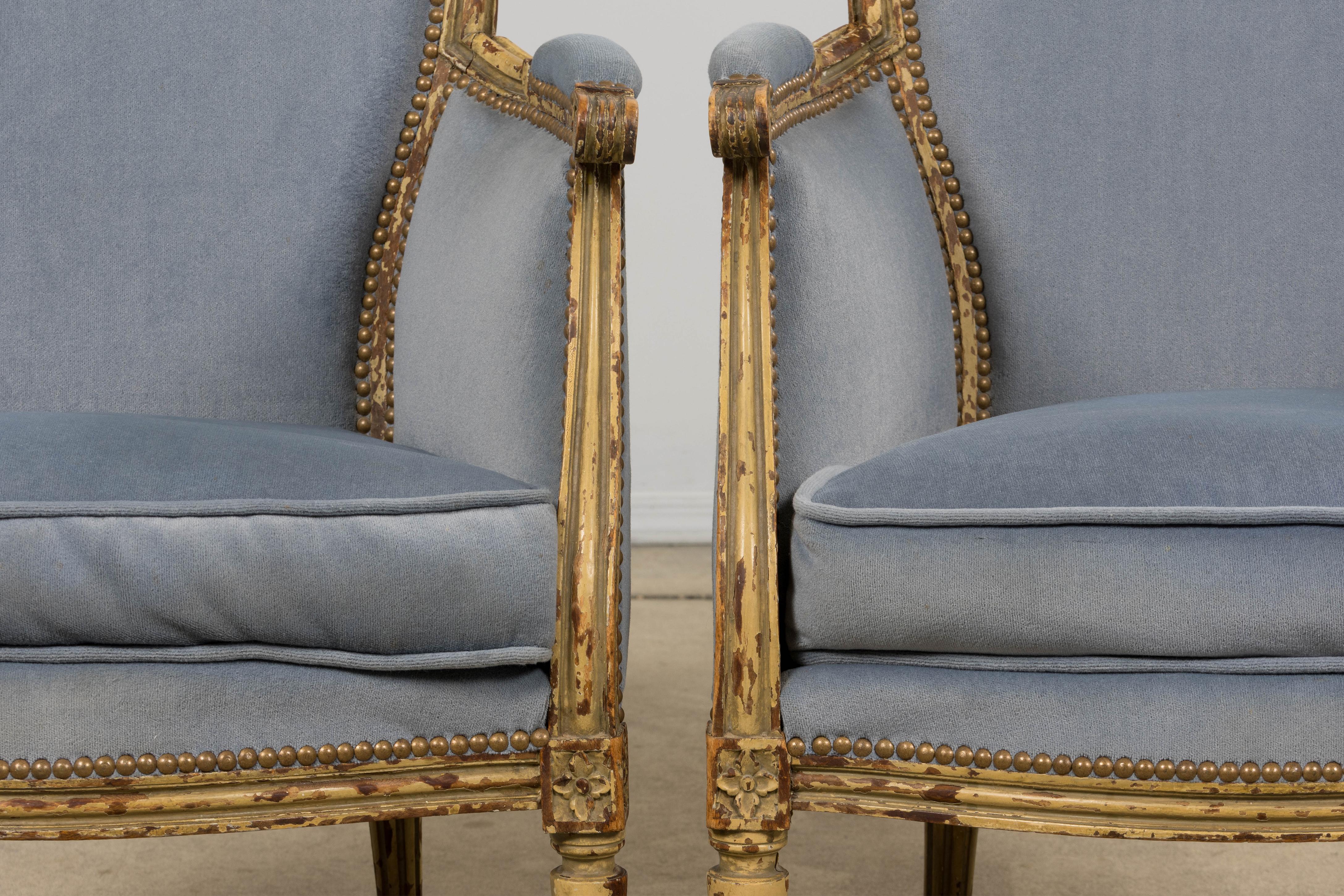 Fina pareja de sillas bergère francesas de estilo Luis XVI de finales del siglo XIX, procedentes de Provenza, Francia. Fabricadas a mano con madera maciza, con armazones restaurados que conservan el acabado original pintado de color crema y