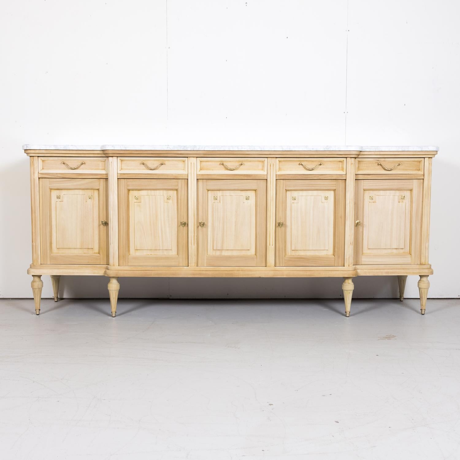 Antique French Louis XVI style bleached enfilade buffet, circa 1920s, having the original thick, moulded and beveled Carrara marble top sitting above five drawers with bronze handles over five doors featuring a step-front design that creates a bit