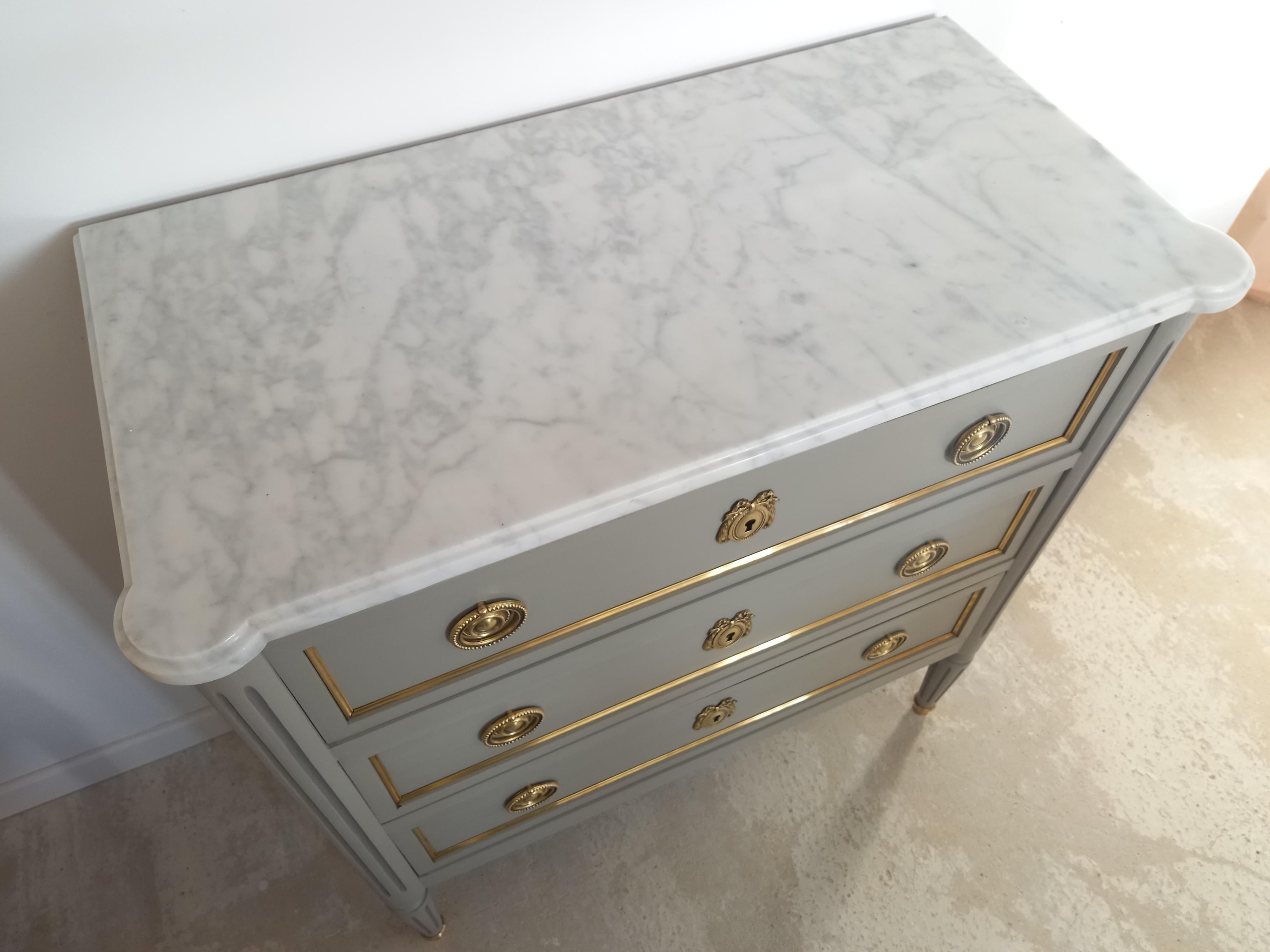 Antique French, Louis XVI style chest of drawers topped with a white Carrara marble, fluted legs finished with golden bronze clogs. 
Three dovetailed drawers with brass details, and three keys.
 
