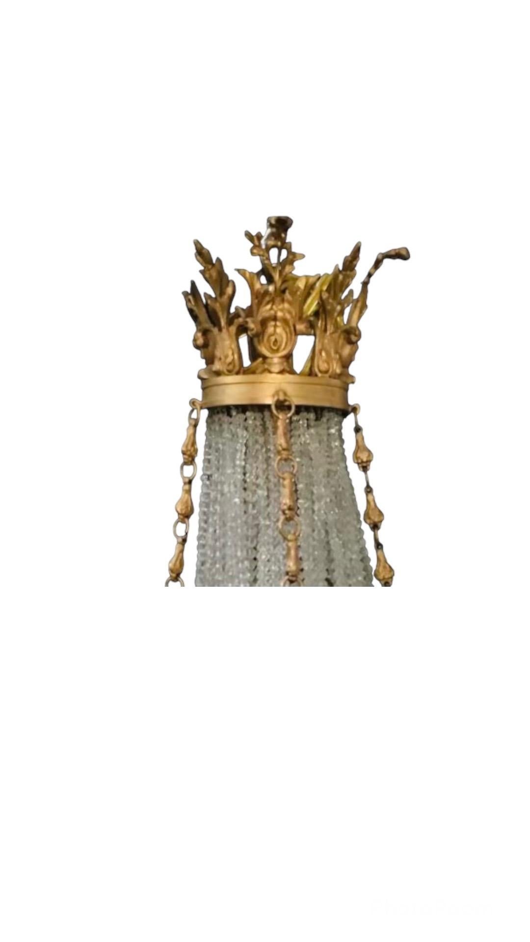 Ce magnifique petit lustre est drapé de cristaux clairs et givrés se terminant par une couronne en bronze Dore. Détails en bronze comprenant des feuilles, des fleurs et des rubans. 

Nombre de lumières : 9