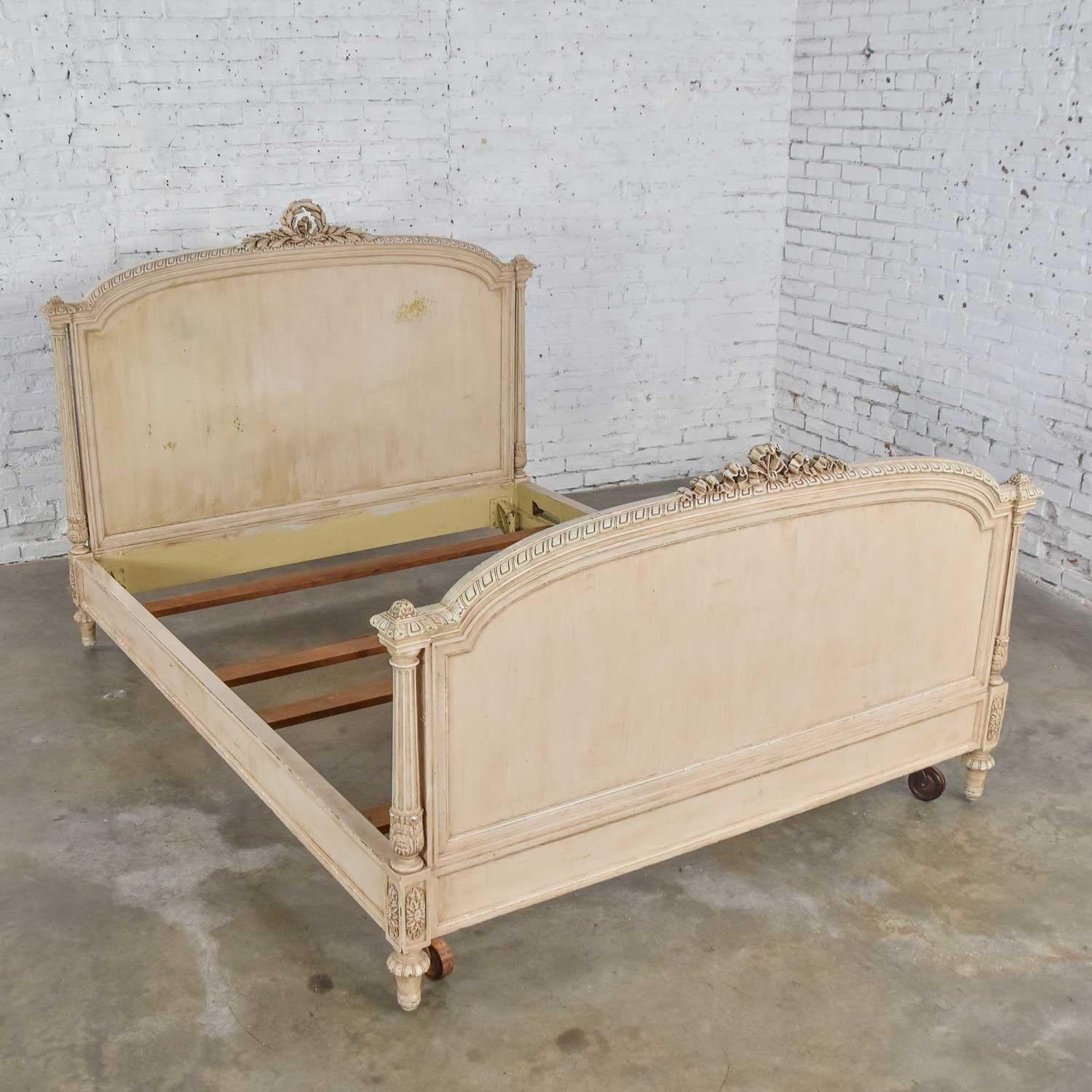 Phenomenal Louis XVI style French off-white painted, antiqued, and distressed queen size bed. Comprised of a carved wood headboard, footboard, side rails, slats, and large wooden casters. Wonderful antique condition with definite nicks and wear in