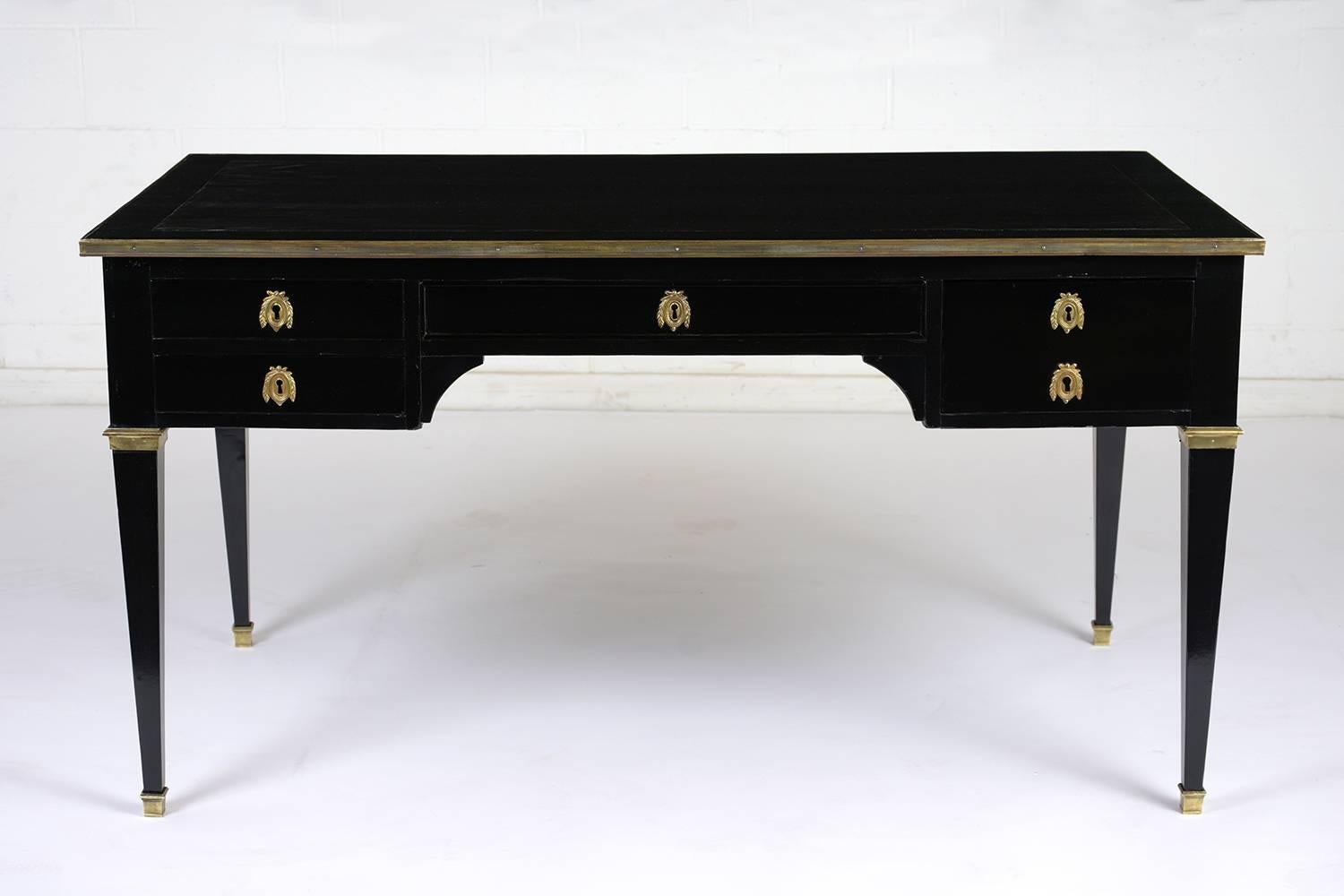 This 1900s French Louis XVI-style desk features an elegant ebonized and lacquered finish. The top of the desk has an embossed leather work area that has been dyed a deep brown color. There are five drawers with ornate brass keyhole plates. Accenting