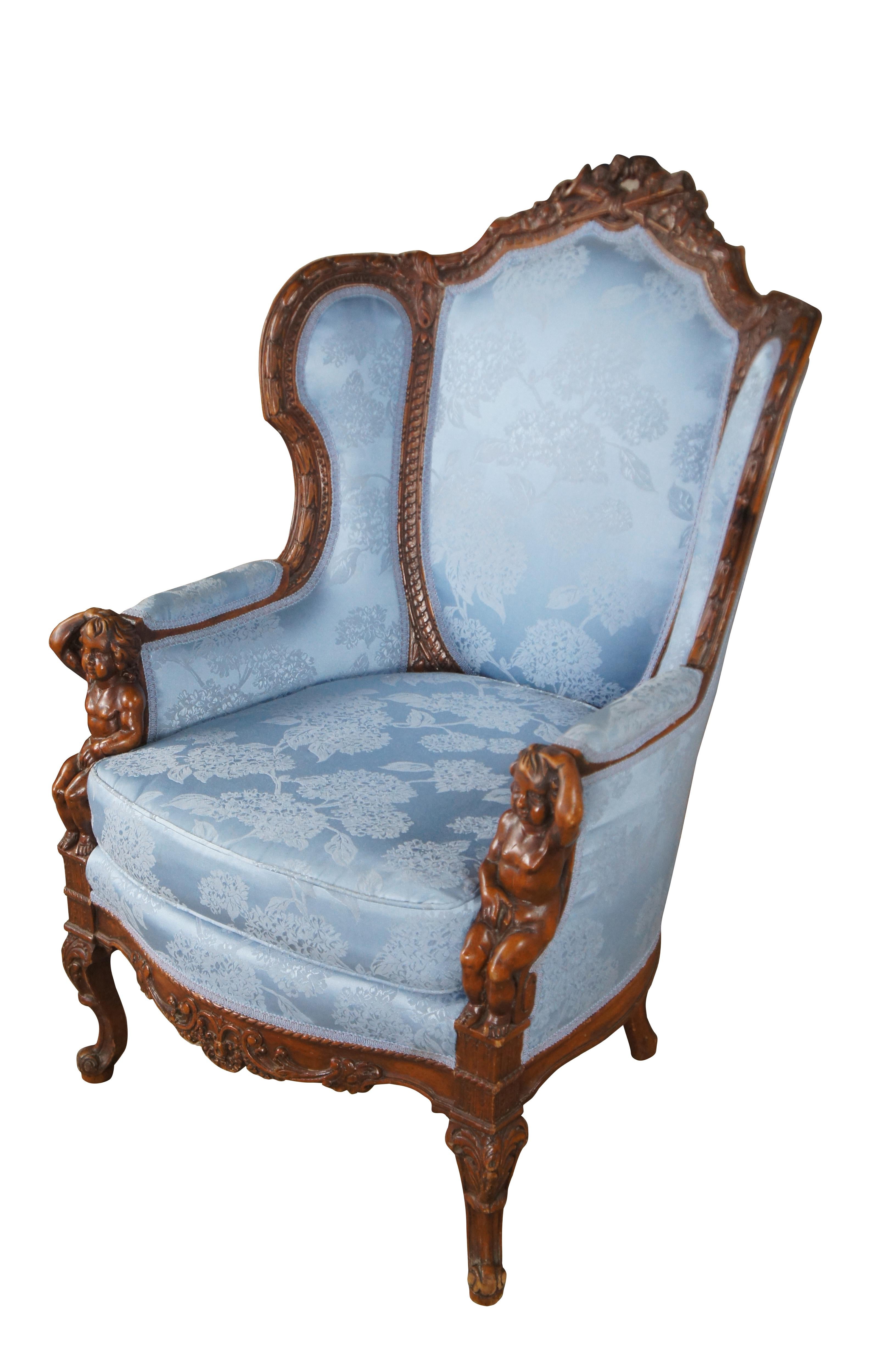 Antique French Louis XVI style Bergere library wingback reading chair, circa 1890-1910.  Made from walnut with a striking pediment featuring a quiver, arrows and torch amongst roses and ribboning.  The pediment is set over a three part silk