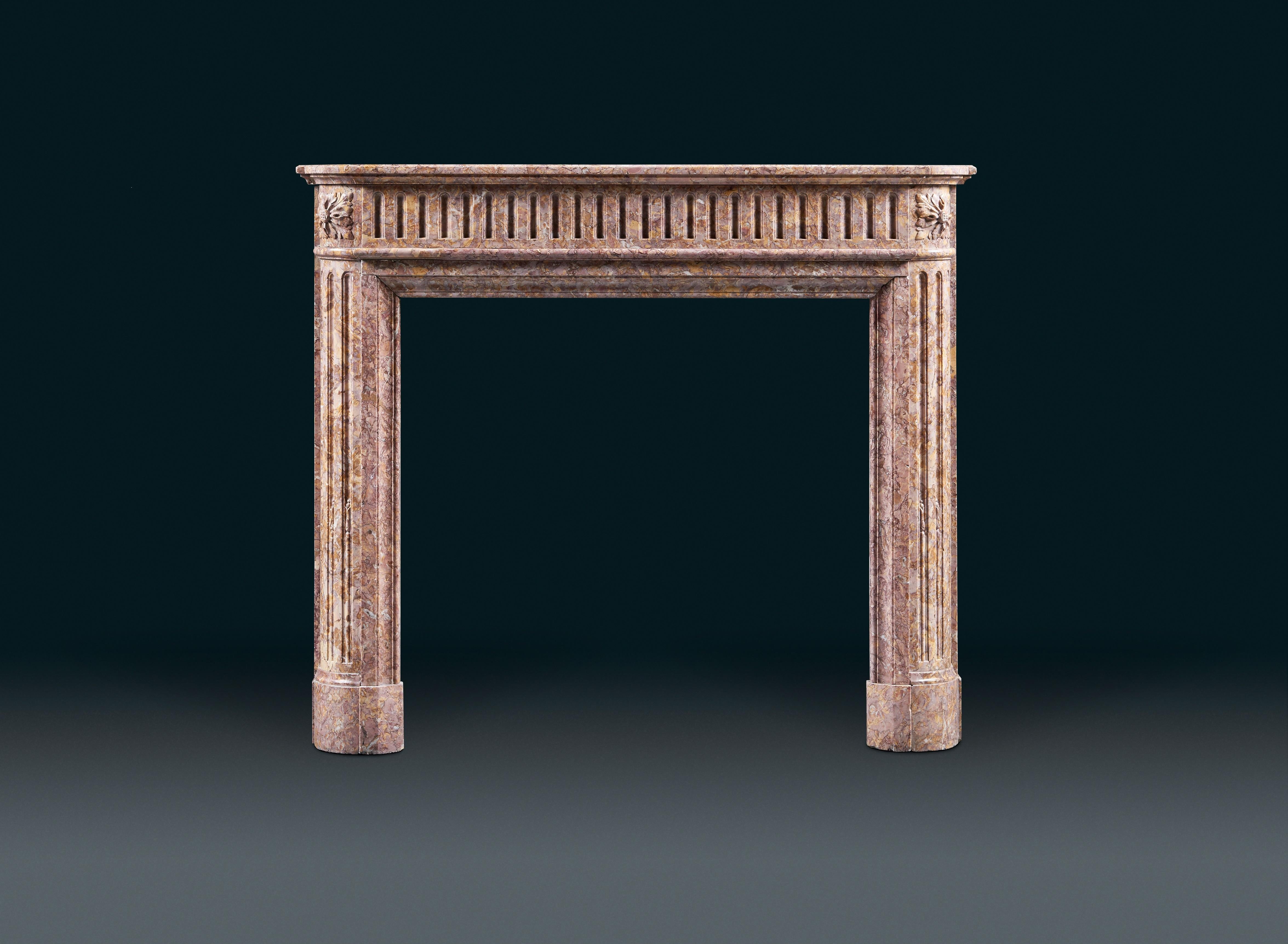 A French 19th century, Louis XVI style antique fireplace mantel in Spanish Brocatello marble. The slightly bowed frieze with continuous finger fluted decoration. The canted jambs with vertical flutes surmounted by carved flower heads.