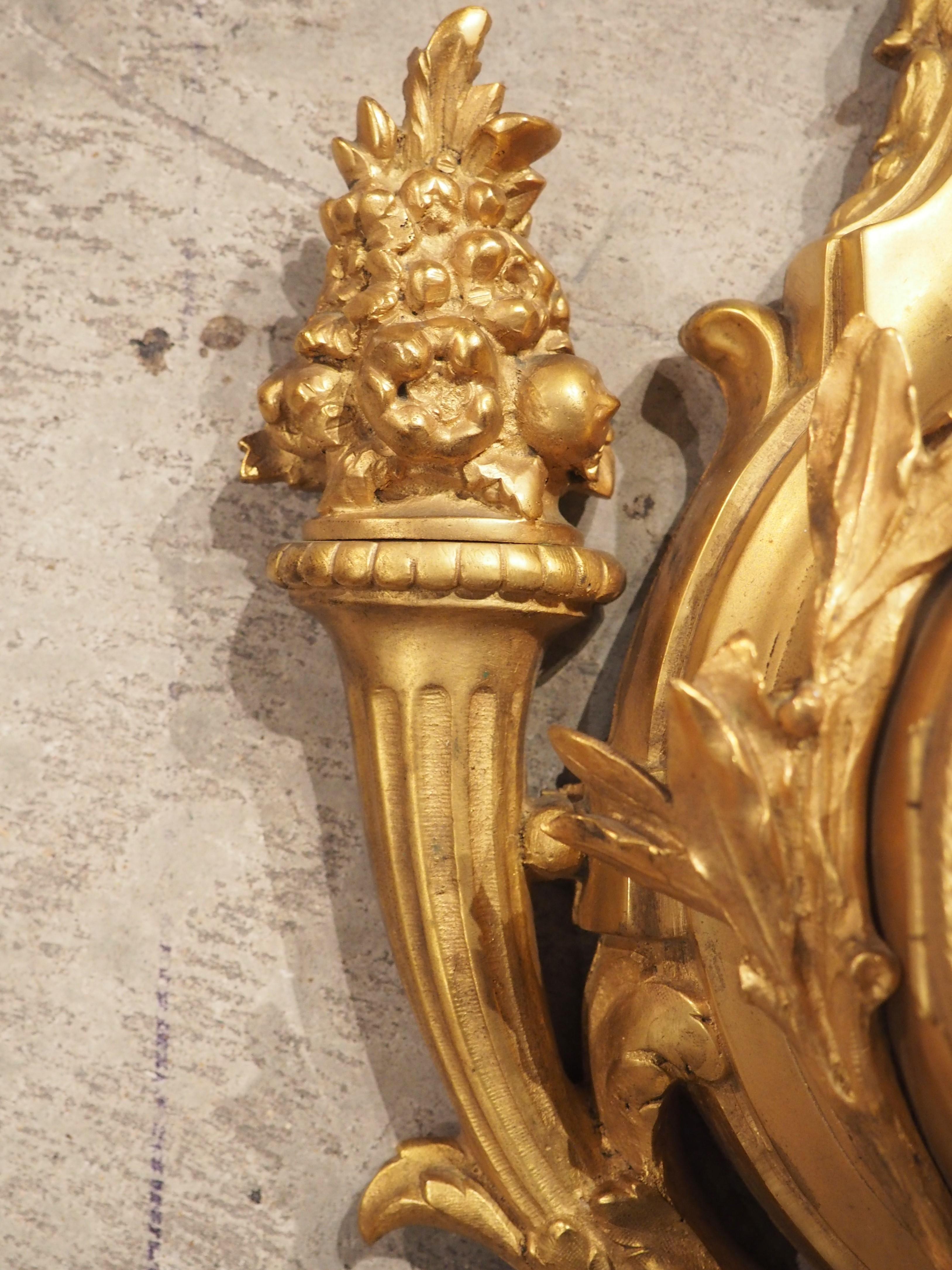 Fabriquée en France dans les années 1800, cette horloge murale en bronze doré de haute qualité présente des éléments de style Louis XVI. Le cadran blanc de l'horloge avec des chiffres bleus repose sur une plate-forme surélevée entourée de feuilles