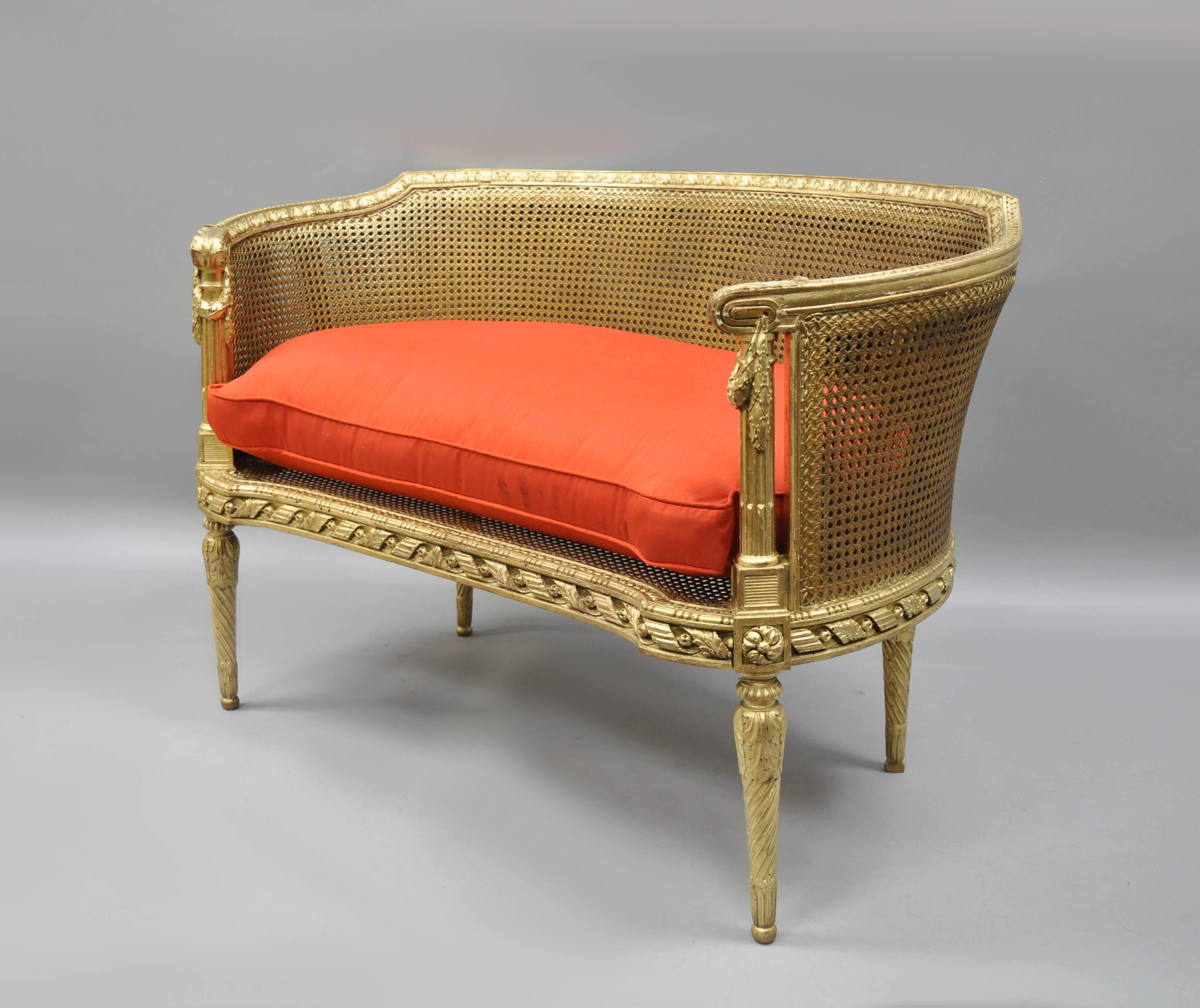 Antique French Louis XVI style gold giltwood parlor settee. Item features a rounded frame, cane back and seat, loose cushion, tapered legs, draped foliage at the arms, finely carved details, and very attractive form. Current finish appears to be a