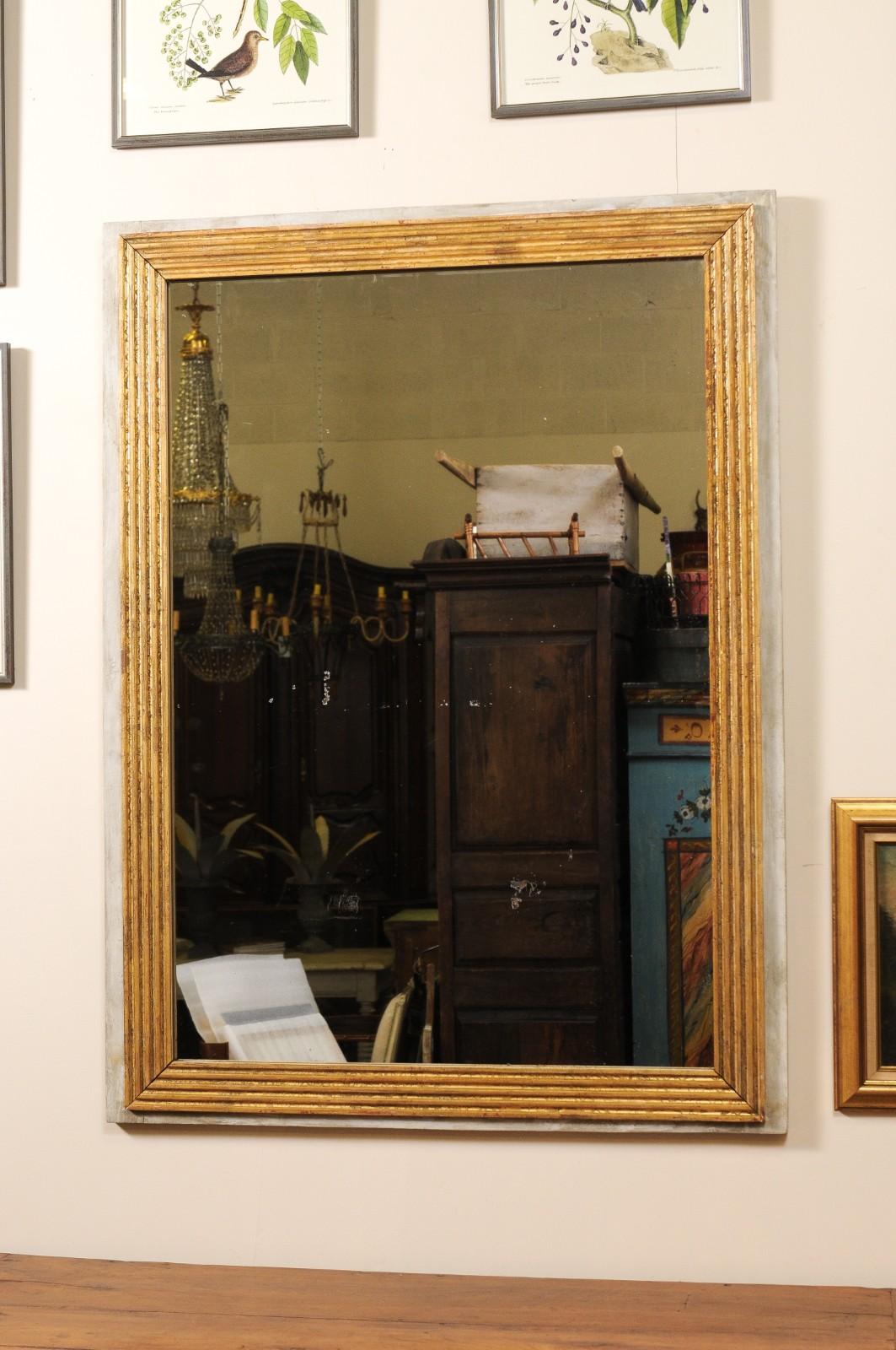 Espejo rectangular de estilo Luis XVI con marco interior de madera dorada, finamente tallado y rodeado de un suave borde gris desgastado por el tiempo. Esta pieza tiene una elegancia discreta y atemporal, y combinaría bien tanto en un espacio