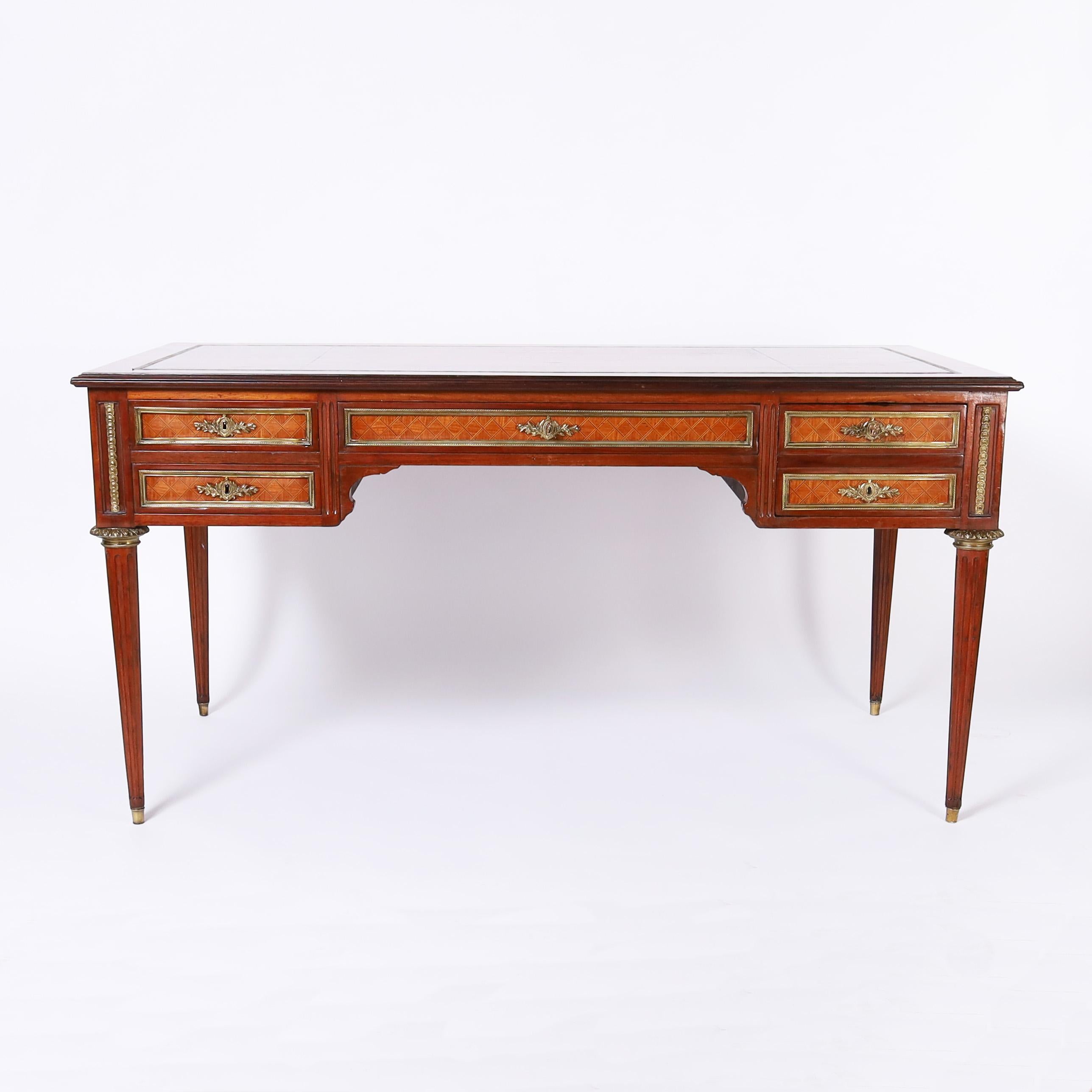 Refined 19th century Louis XVI style desk featuring the original tooled leather top on a case with three drawers in the front and the reverse of the desk with false drawers, geometric marquetry panels, bronze ormolu, a hidden compartment, working