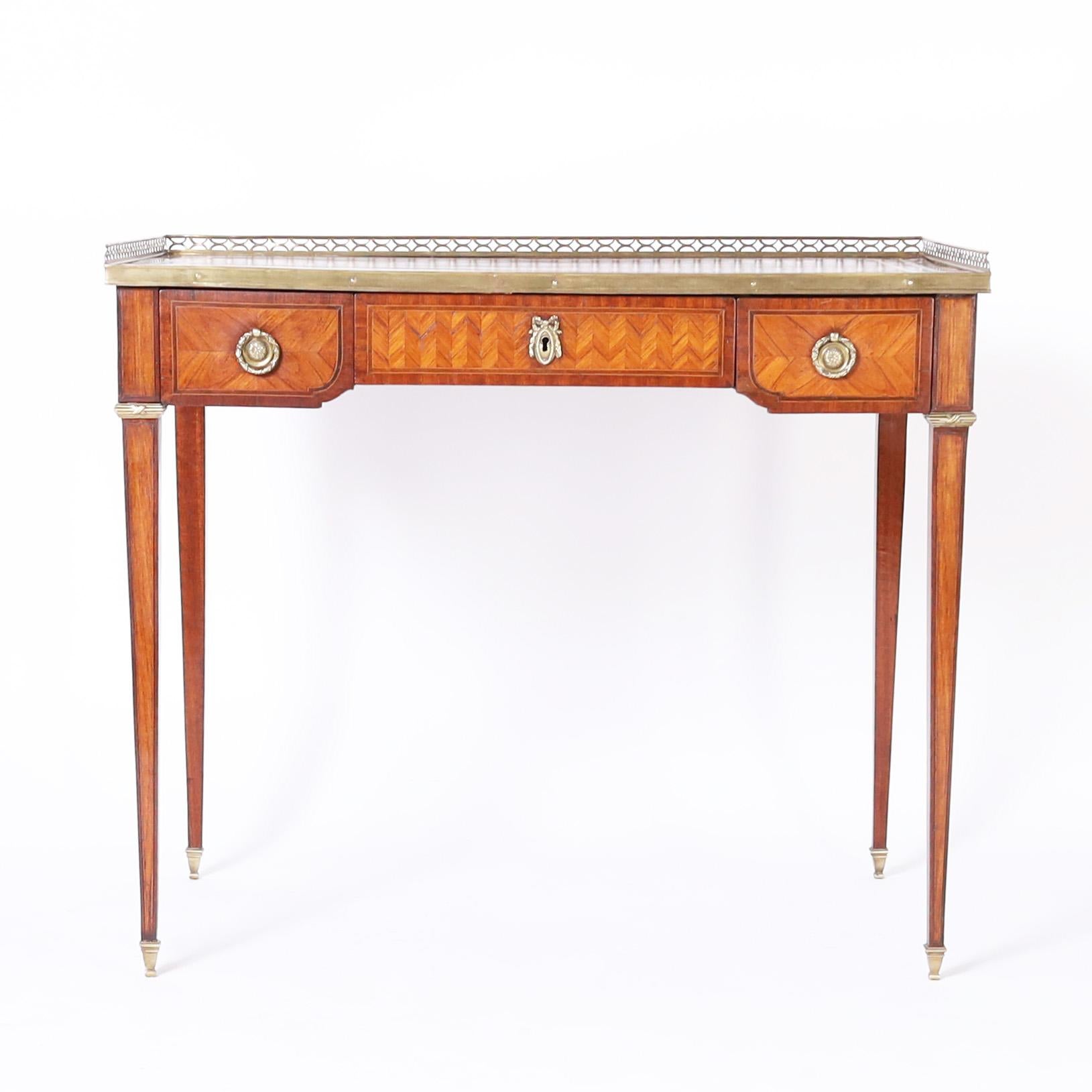 Refined antique French Louis XVI style writing desk crafted in exotic tulipwood veneer with crossbanding and chevron designs, having a tooled leather top with a brass gallery, the case has three drawers and is supported by long elegant tapered legs