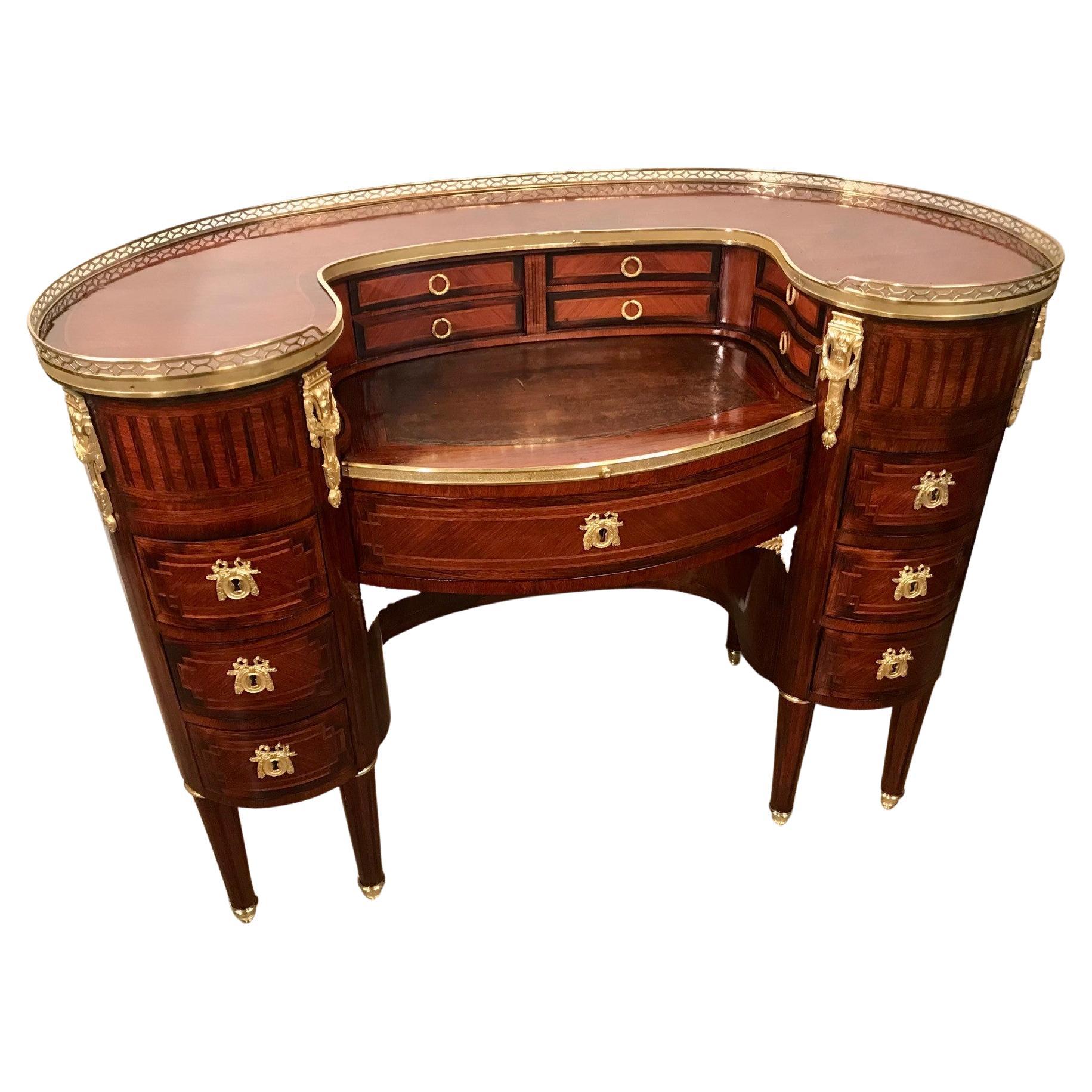 Although of kidney shape, this desk is more substantial than generally found in such a form. The top has a pierced brass gallery enclosing a fanning kingwood veneer. The leather slide-out writing surface is enclosed by a pair of tambour shutters
