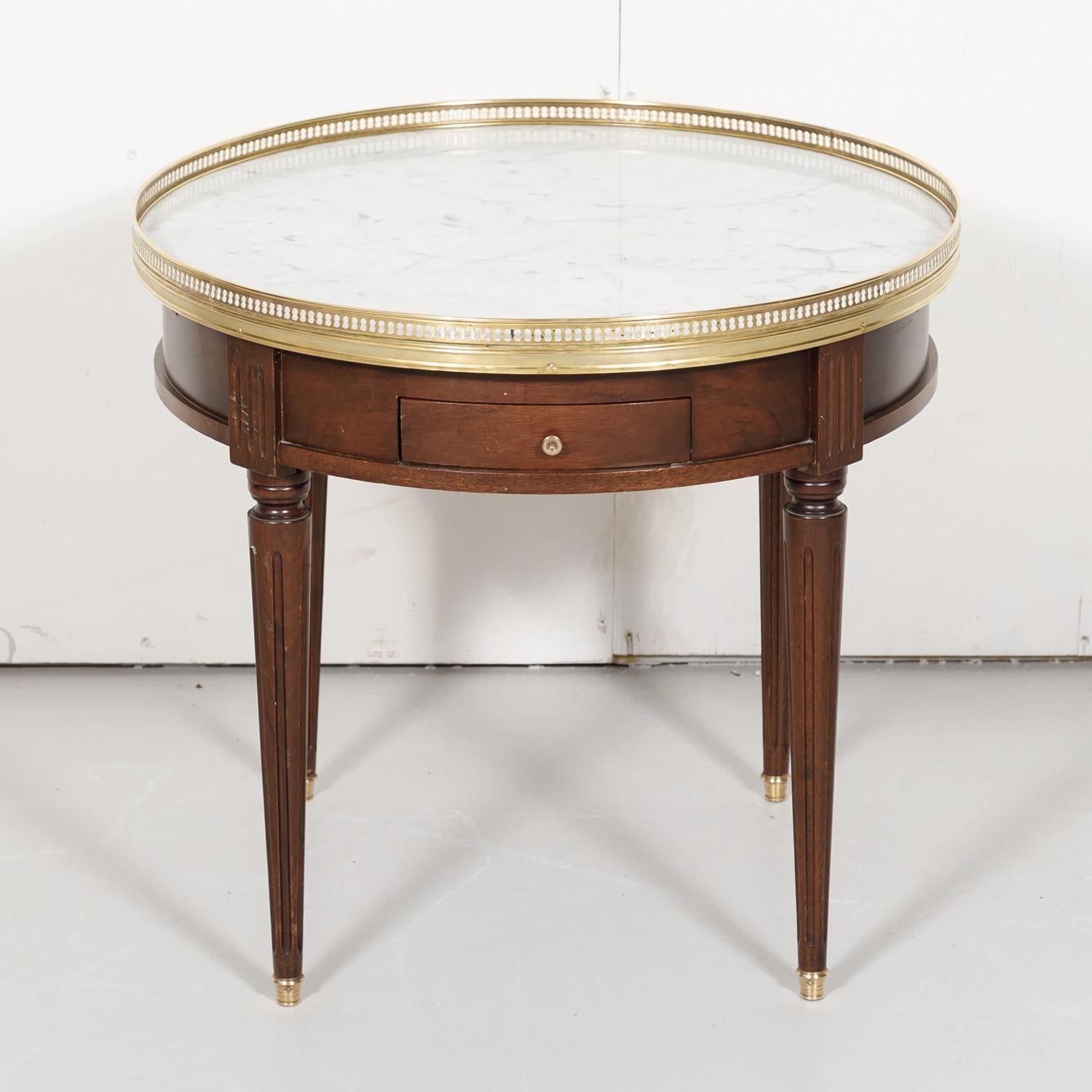 Classic Louis XVI style bouillotte side table in mahogany with a Carrara marble top surrounded by a pierced brass gallery, circa early 1900s. The apron has a drawer for cards and chips and two slides with embossed leather tops that were originally