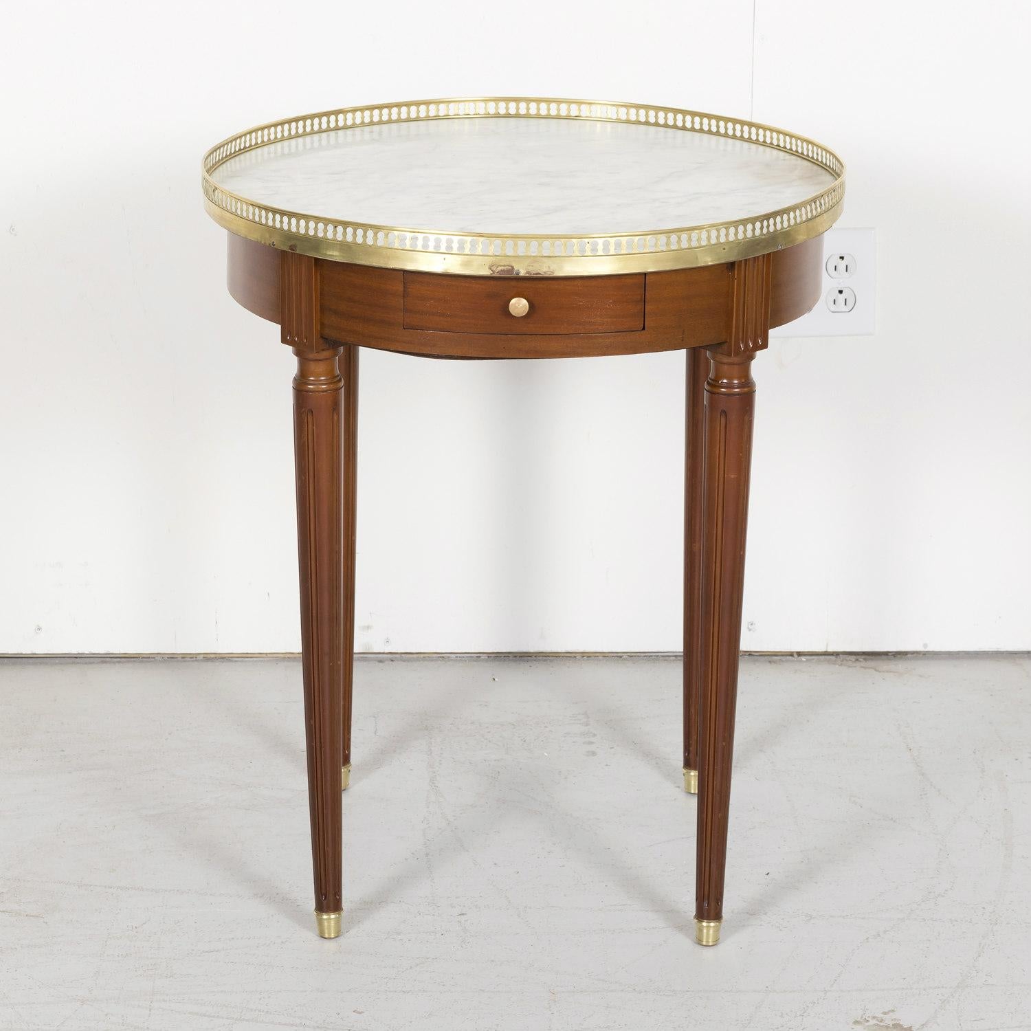 Antique French Louis XVI style bouillotte side table handcrafted of mahogany near Paris, circa 1900. Having a white Carrara marble top surrounded by a pierced gilt brass gallery, this handsome French side table features an apron that has a single