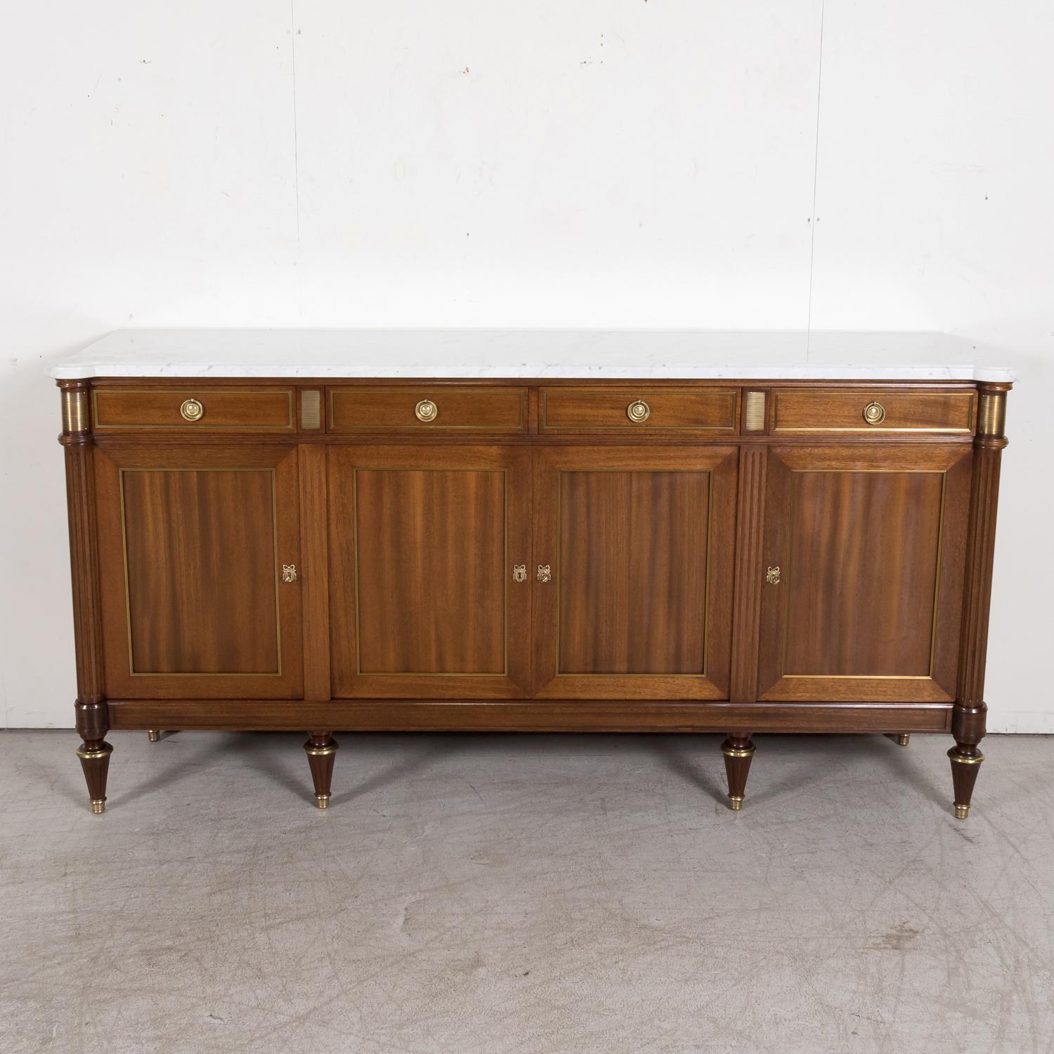 A beautiful early 20th century antique French Louis XVI style enfilade buffet handcrafted of mahogany by skilled artisans in Paris, circa 1920s, having a moulded edge white Carrara marble top with cookie cutter corners above four drawers over four