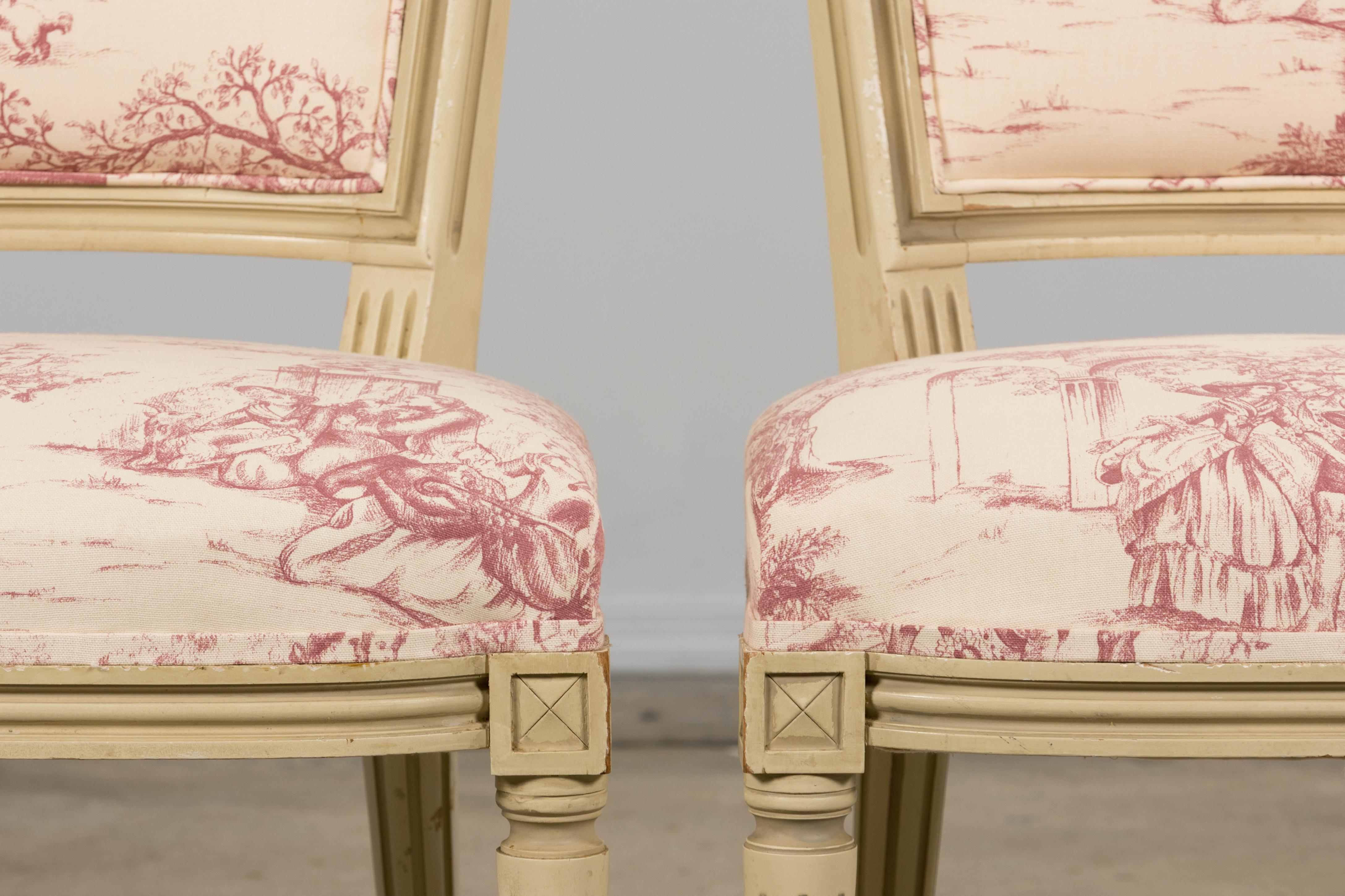 An exquisite pair of restored antique French accent side chairs in the Marie Antoinette/Louis XVI style, sourced from Provence, France. These chairs feature finely hand-carved shield-shaped backrests, finished in creamy antique white paint with a