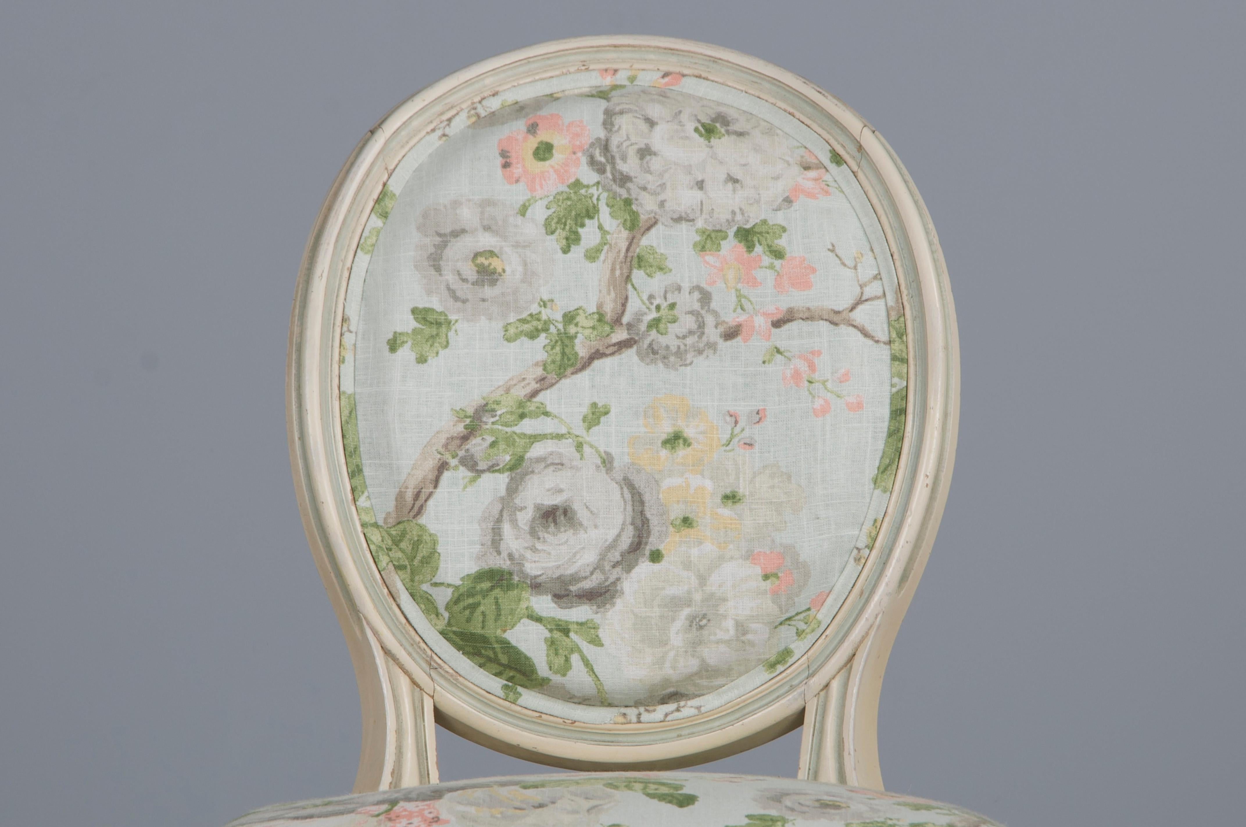 Preciosa silla auxiliar antigua de estilo Luis XVI, procedente de la Provenza francesa. La silla tiene un armazón artesanal con respaldo ovalado, pintado en un blanco cremoso con toques azules que muestra una pátina envejecida de forma natural con