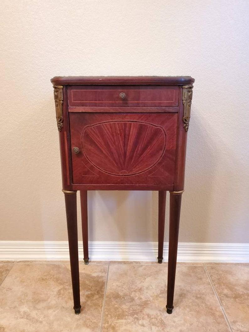 A stunning antique Louis XVI style bedside cabinet with outstanding patina. Hand crafted in France during the late 19th / early 20th century, having a marble-top on a parquetry and stringwork inlaid case with decorative gilt-metal accents, single