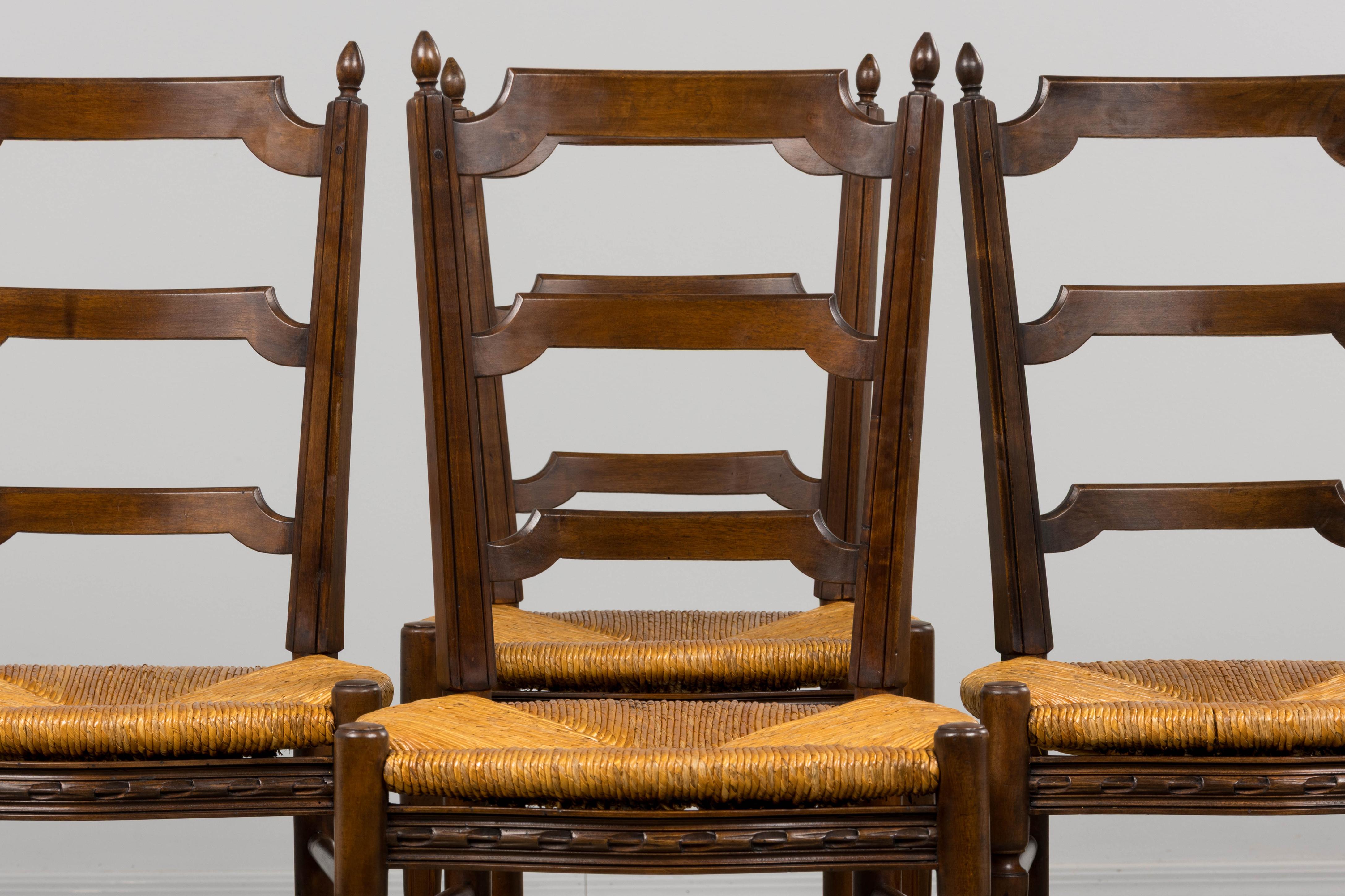 An exquisite set of eight late 19th century French country dining chairs in Louis XVI style, sourced in Provence. Crafted in solid walnut, each chair features a tall ladder-back with three shaped horizontal splats and turned finials crowning the