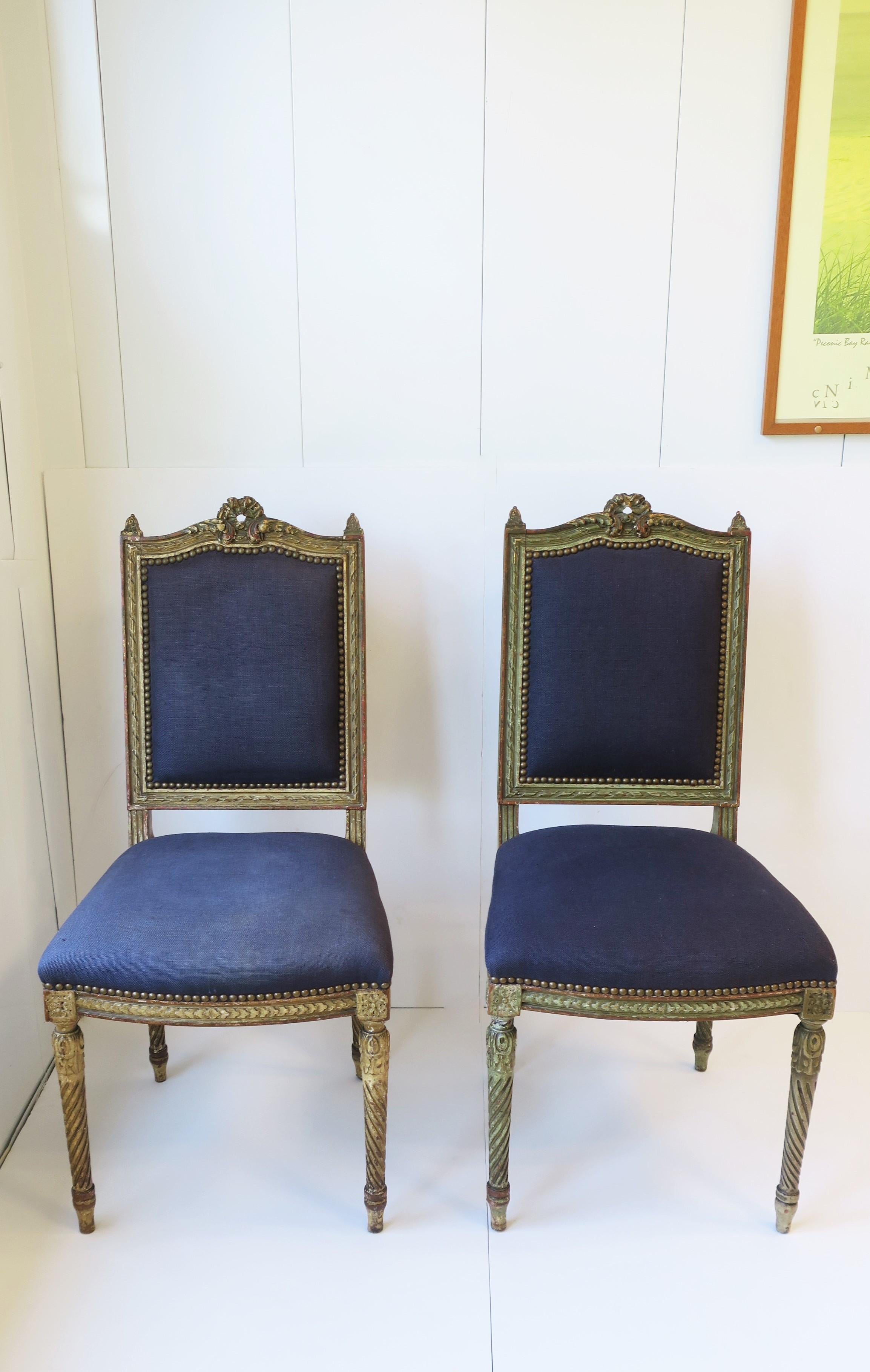 A pair of antique French Louis XVI blue and gold gilt side, desk, hall or dining chairs, circa late-19th Century, France. At some point chairs were reupholstered; shown here with a blue linen fabric finished off with a matte brass nail head design.